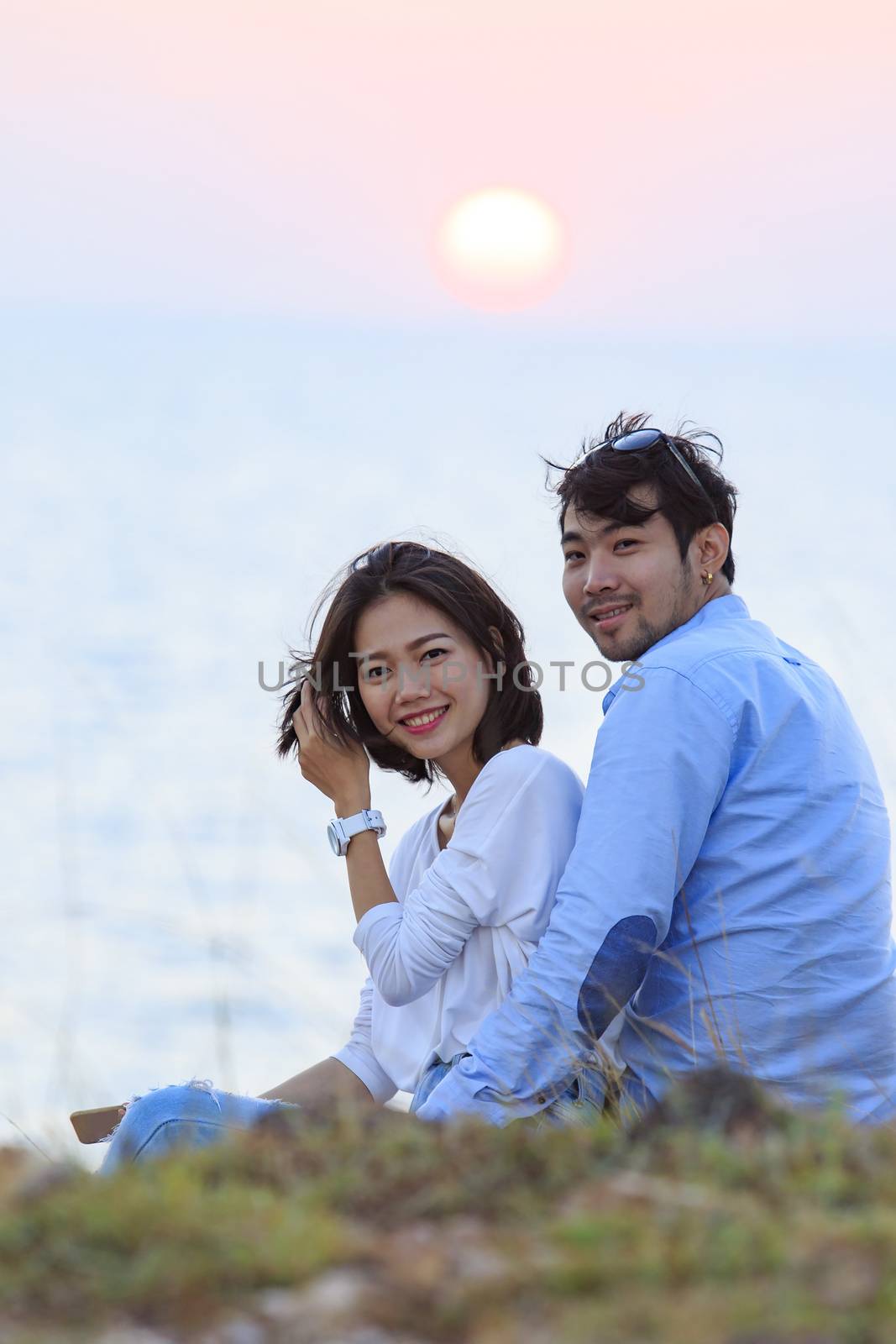 portrait of asian younger man and woman relaxing vacation at sea side happiness emotion against sun set sky background