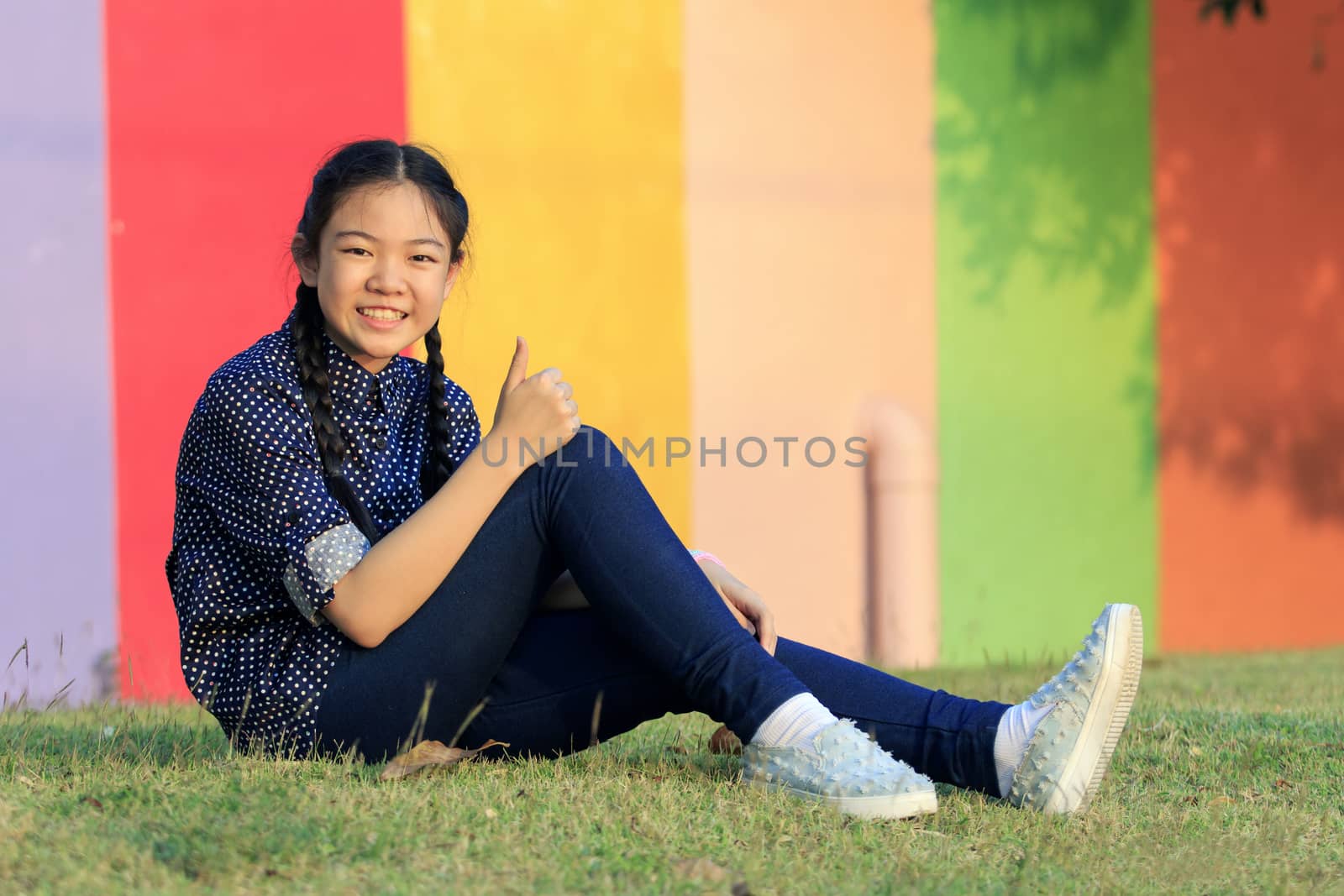 asian girl relaxing sitting on green grass field of public park and hand sign ok ,all right with toothy smiling face happiness emotion