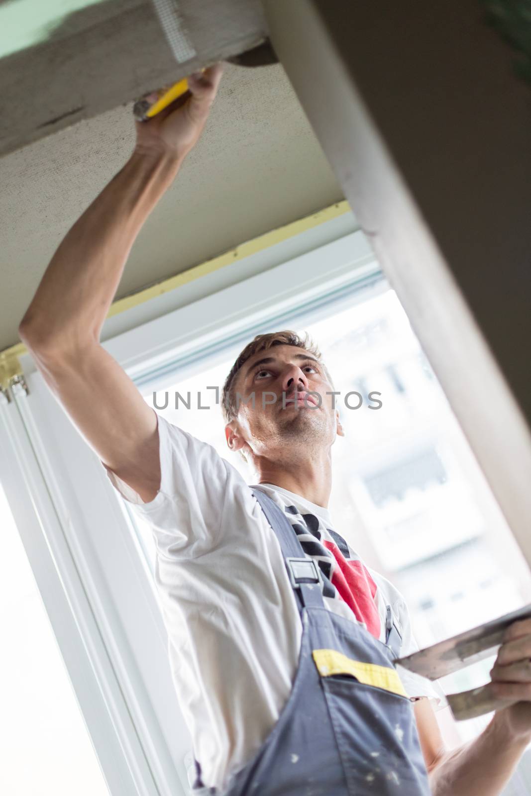 Thirty years old manual worker with wall plastering tools renovating house. Plasterer renovating indoor walls and ceilings with float and plaster.