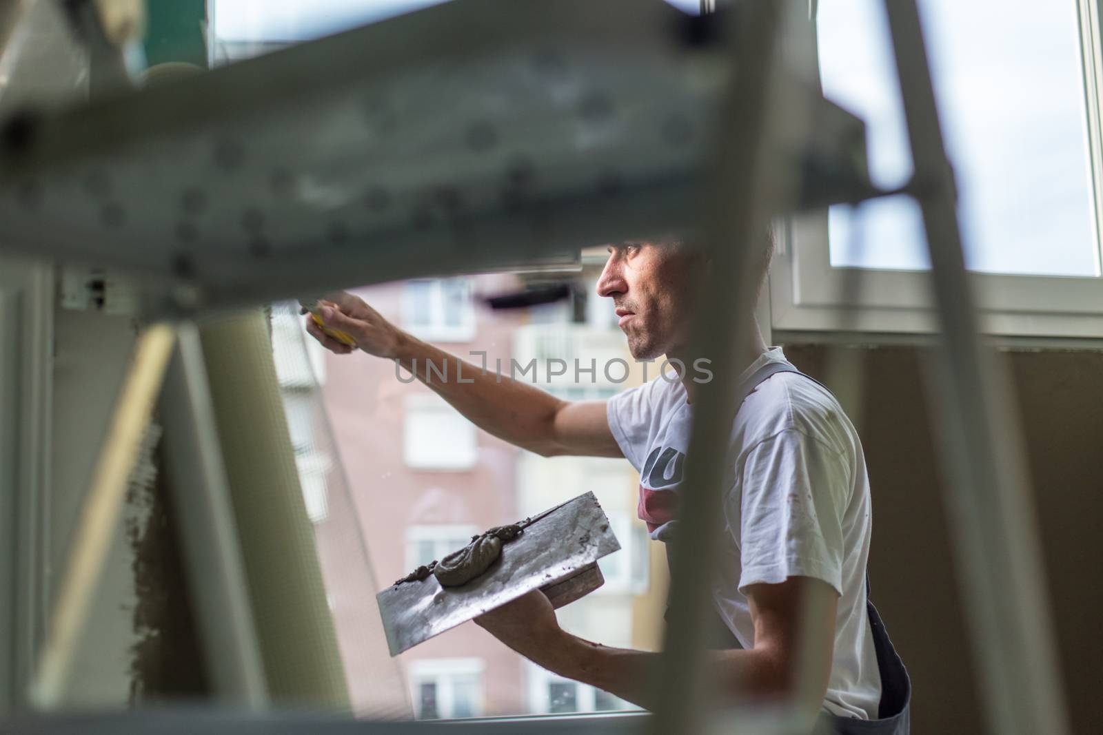 Thirty years old manual worker with wall plastering tools inside a house. Plasterer renovating indoor walls and ceilings with float and plaster.