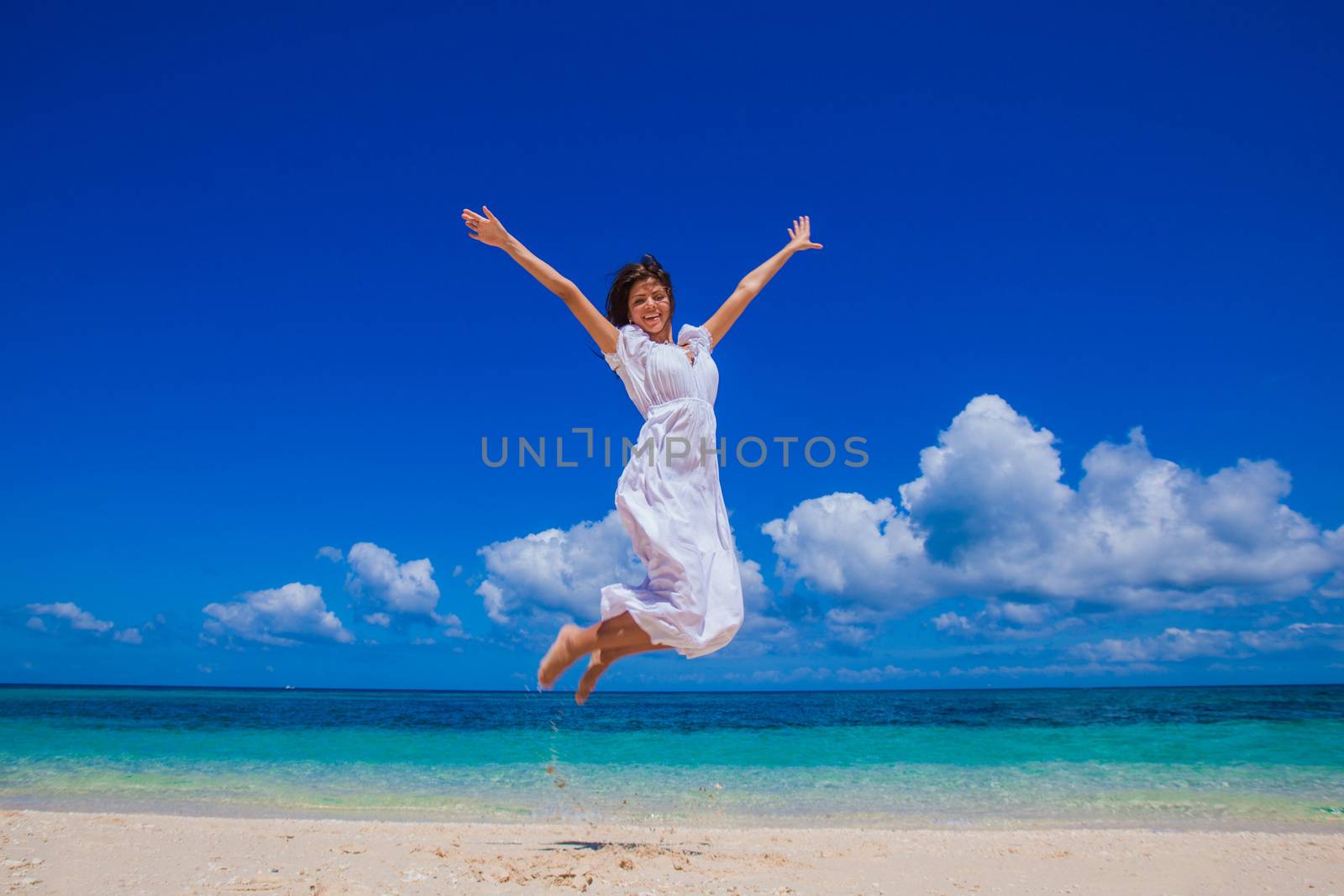 Happy young woman in white dress jumping on the beach