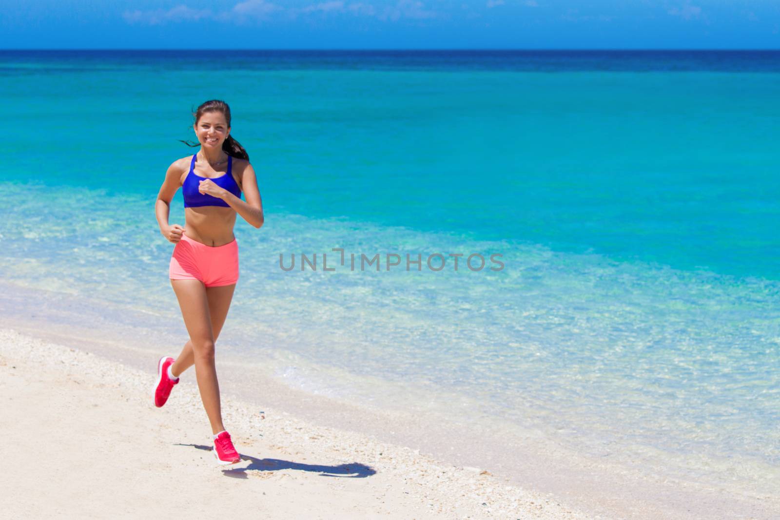Beautiful young fitness woman running on beach