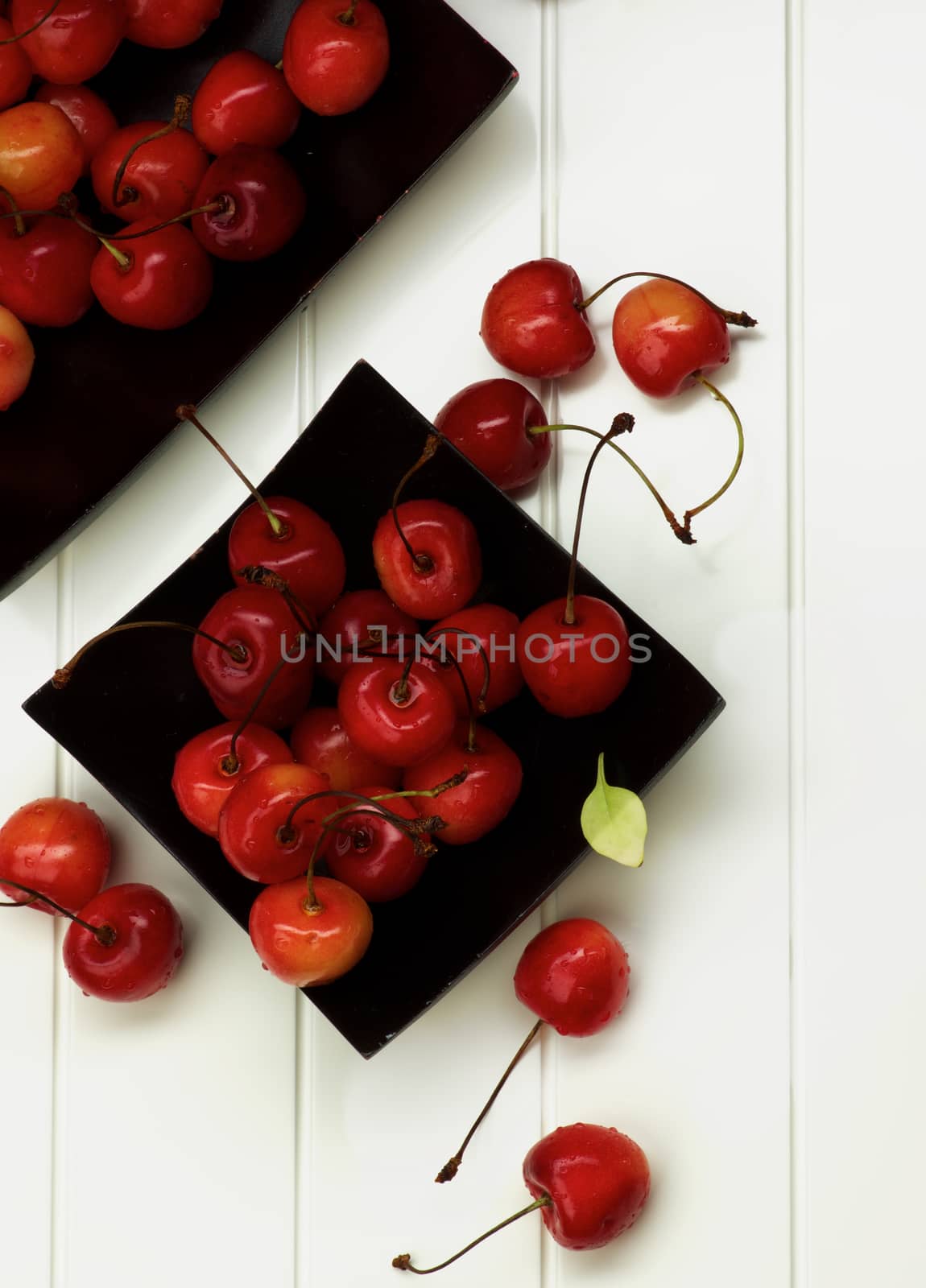 Arrangement of Two Black Plates with Fresh Ripe Sweet Maraschino Cherries closeup on Plank White background. Top View