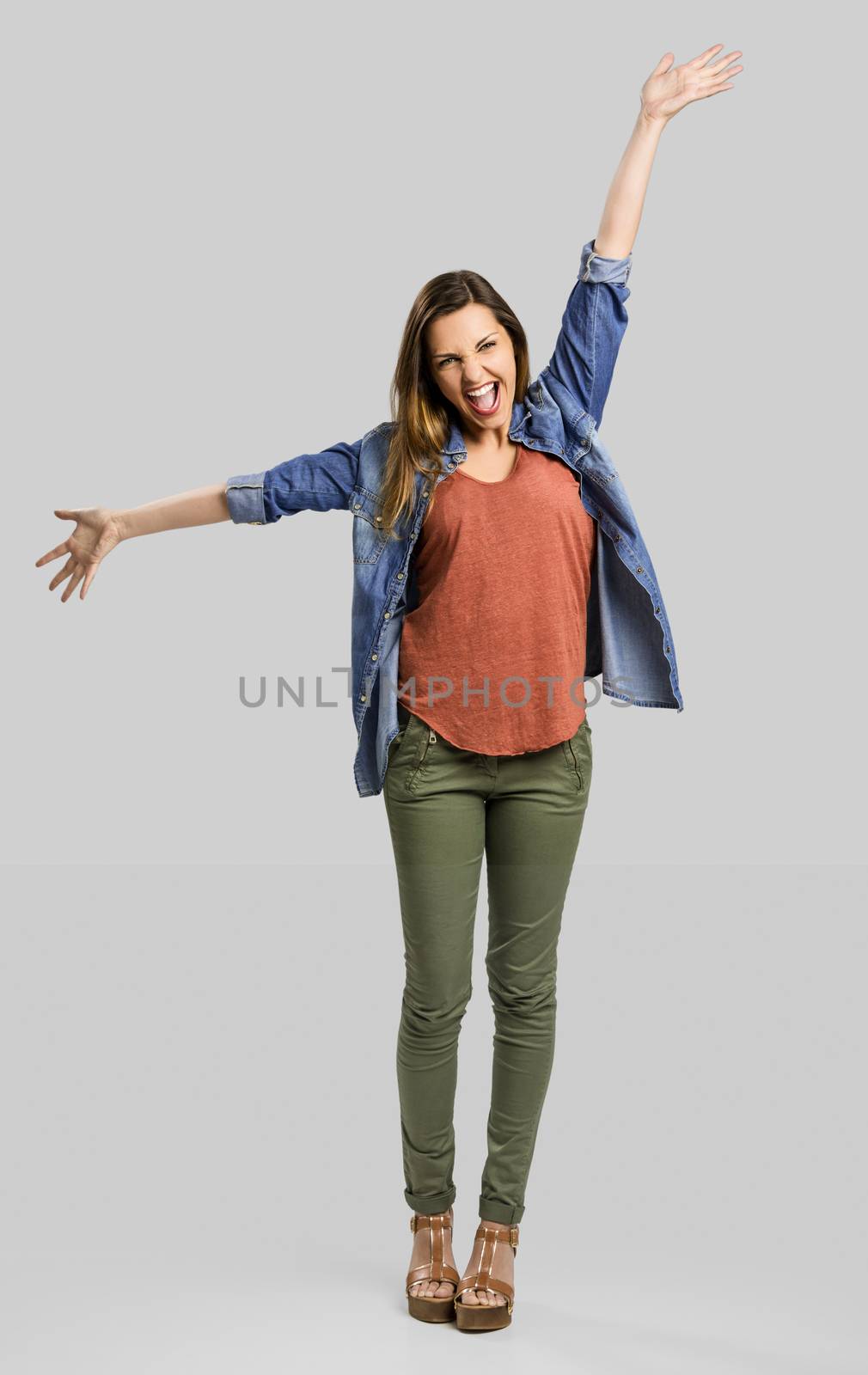 Beautiful happy woman with arms up over a gray background