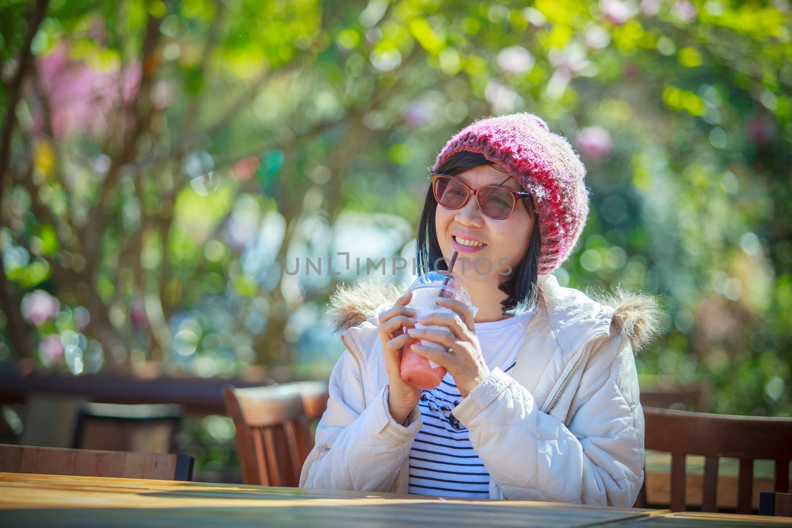 portrait of 40s years asian woman with cool juicy drinking bottle in hand with happiness emotion sitting in beautiful park background