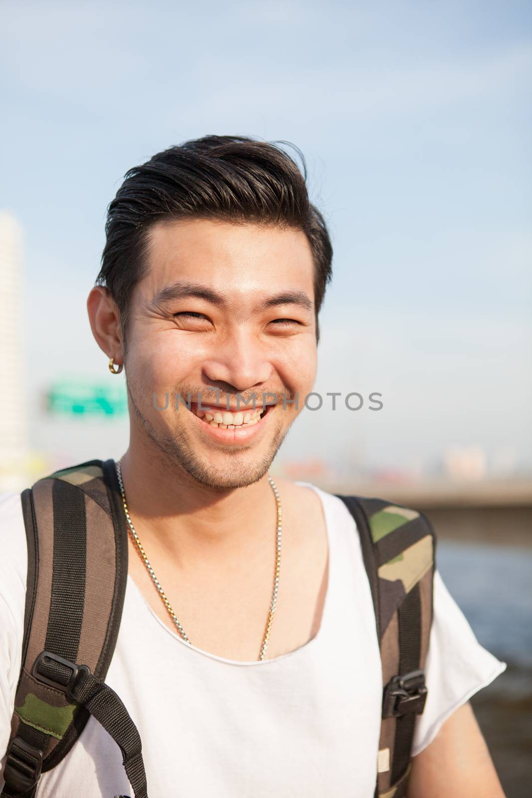 portrait of traveling with backpacker asian man toothy smiling face , laughing with happiness emotion outdoor