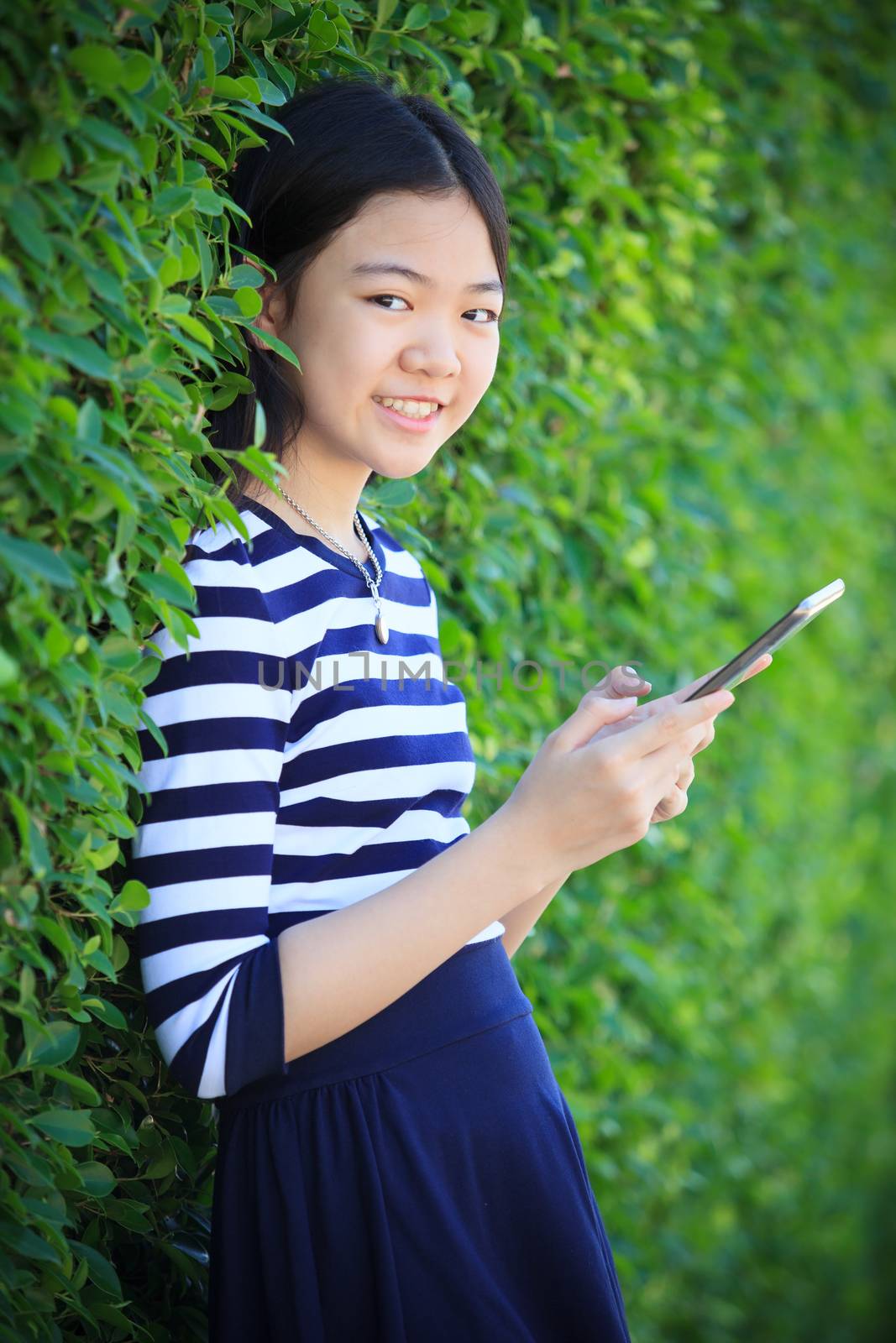 portrait of asian teen age ,girl with computer tablet in hand standing against green garden with happiness and relax emotion outdoor use for modern digital lifestyle
