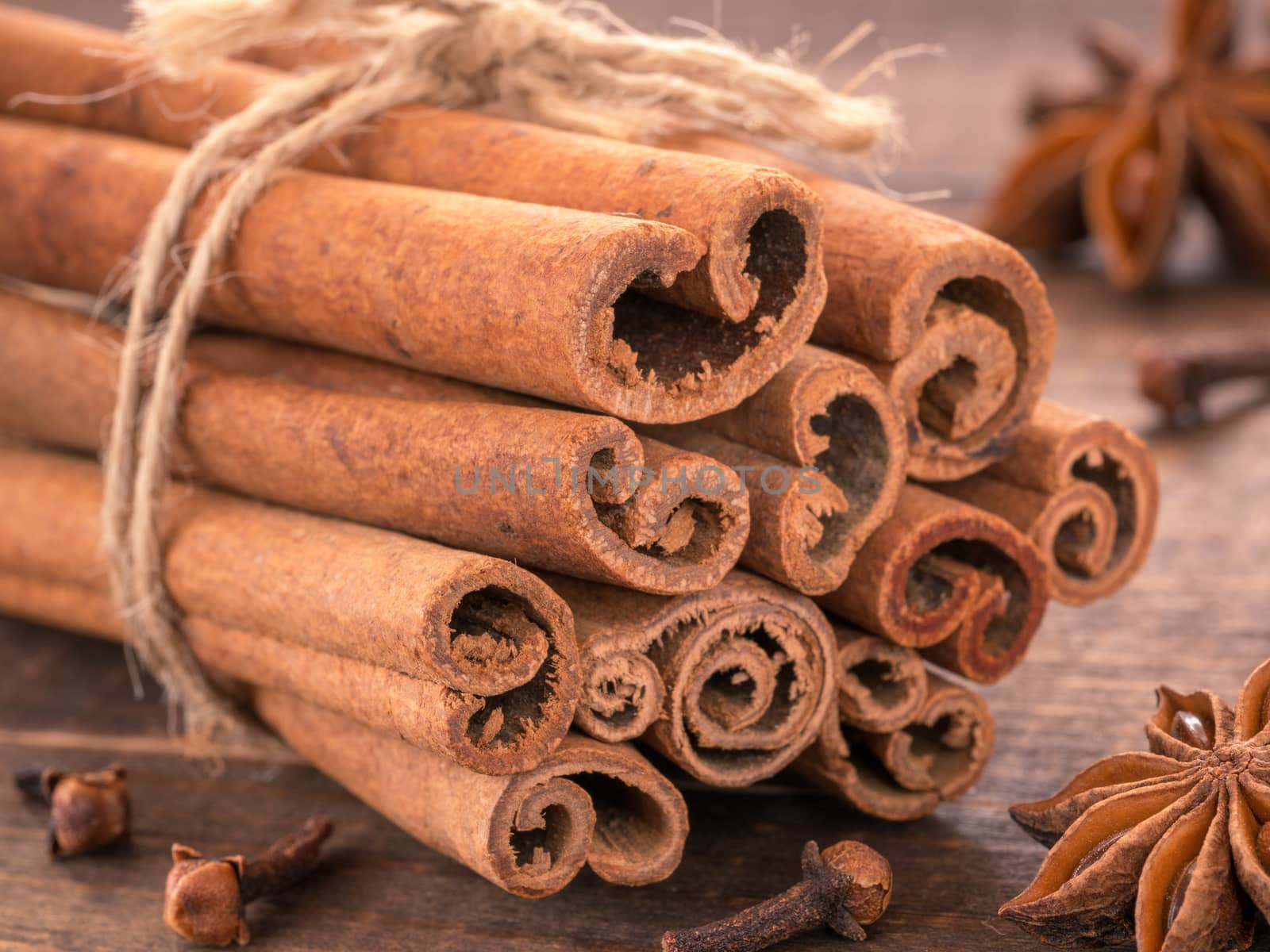 Ground cinnamon, cinnamon sticks, tied with jute rope on wooden background. Clove and star anise as background