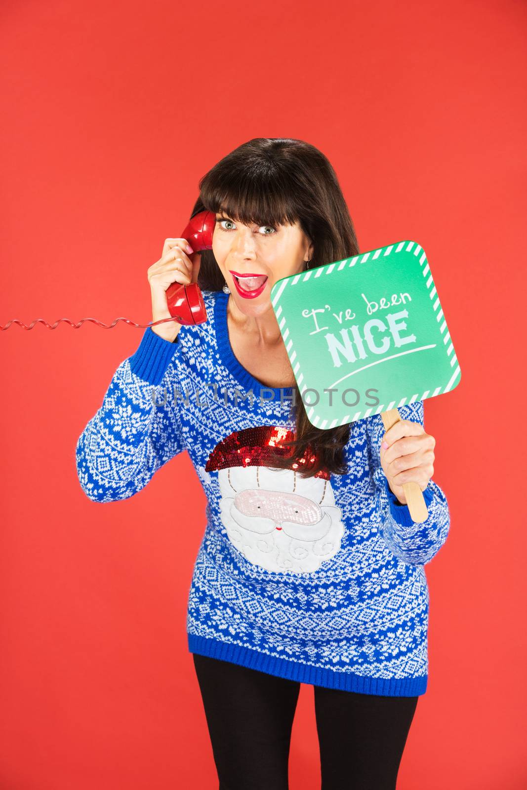 Excited woman in ugly blue Santa sweater holding green nice sign while on phone