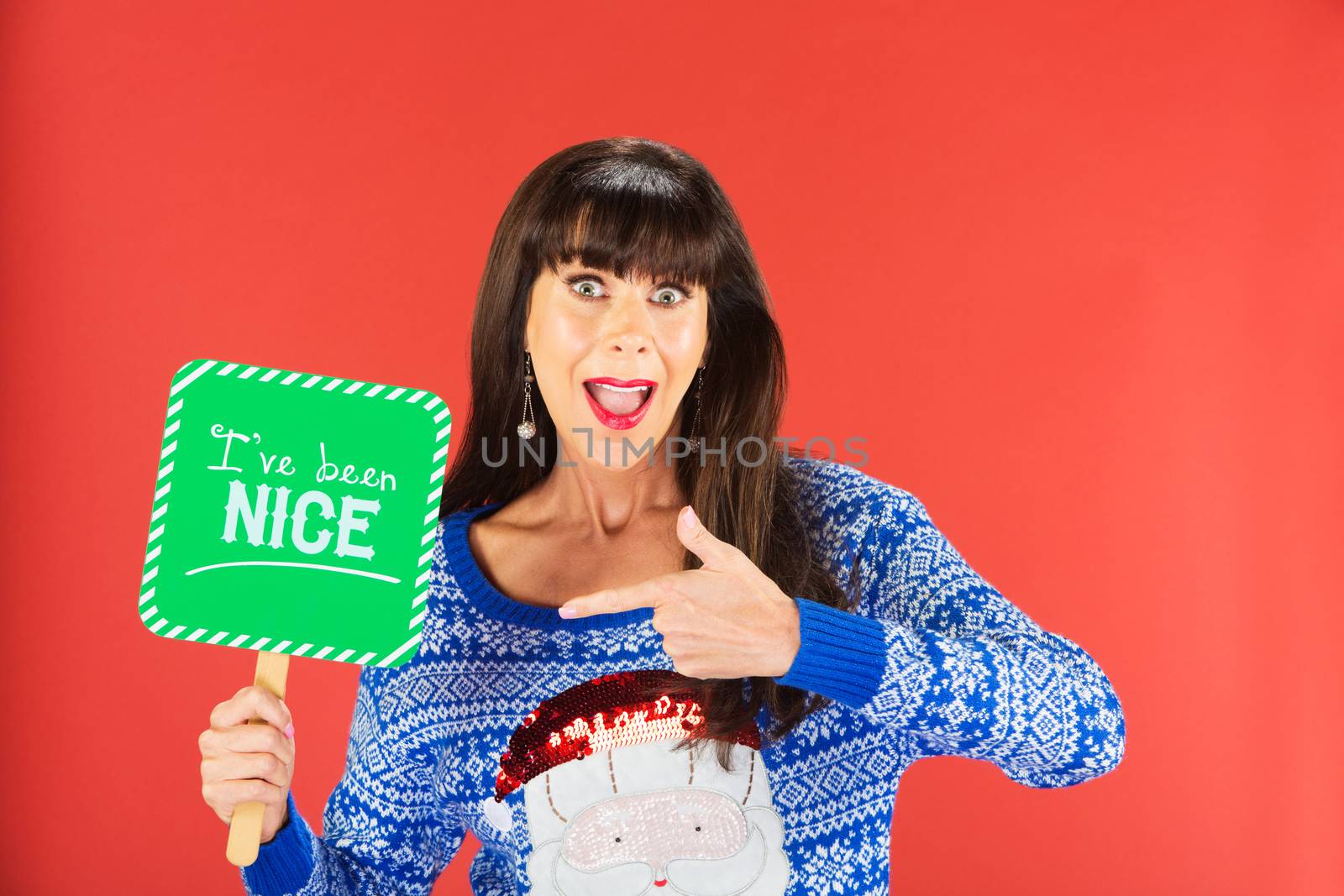 Happy single woman in ugly knitted sweater pointing to nice sign over red background