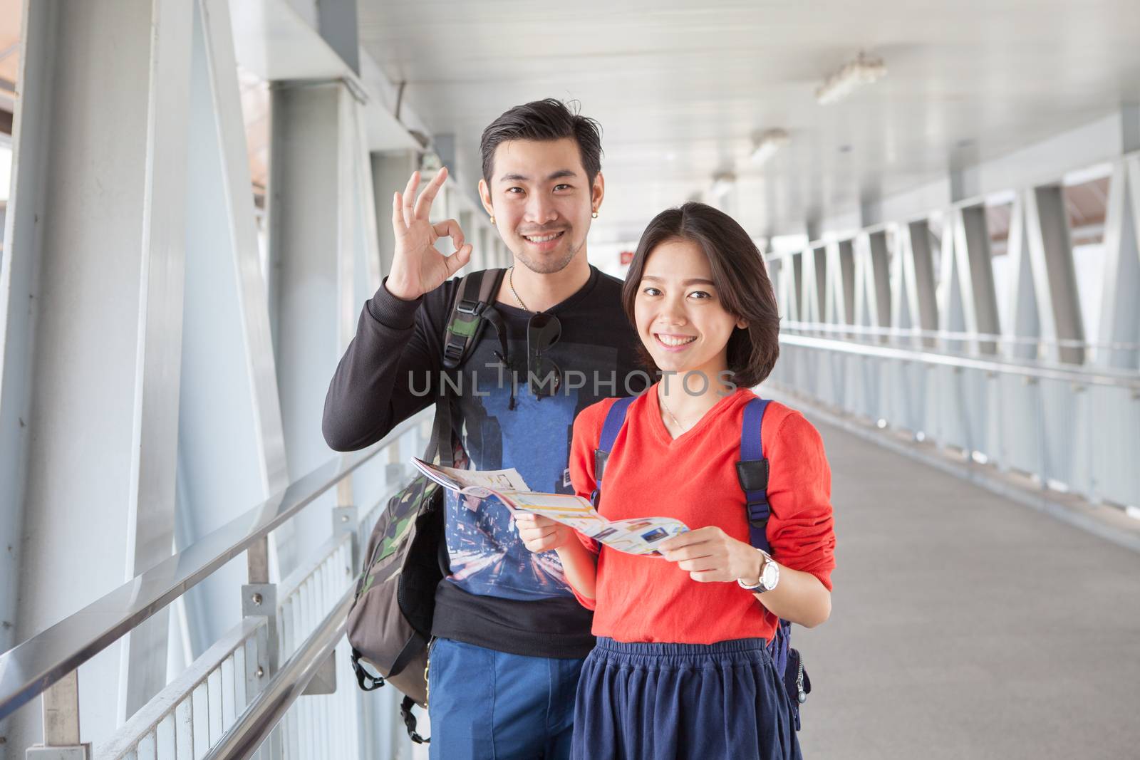 younger asian traveling man and woman standing with toothy smili by khunaspix