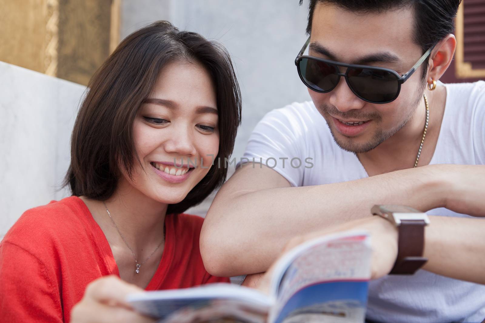 couples of asian younger traveling man and woman reading a guide book with happiness face toothy smile