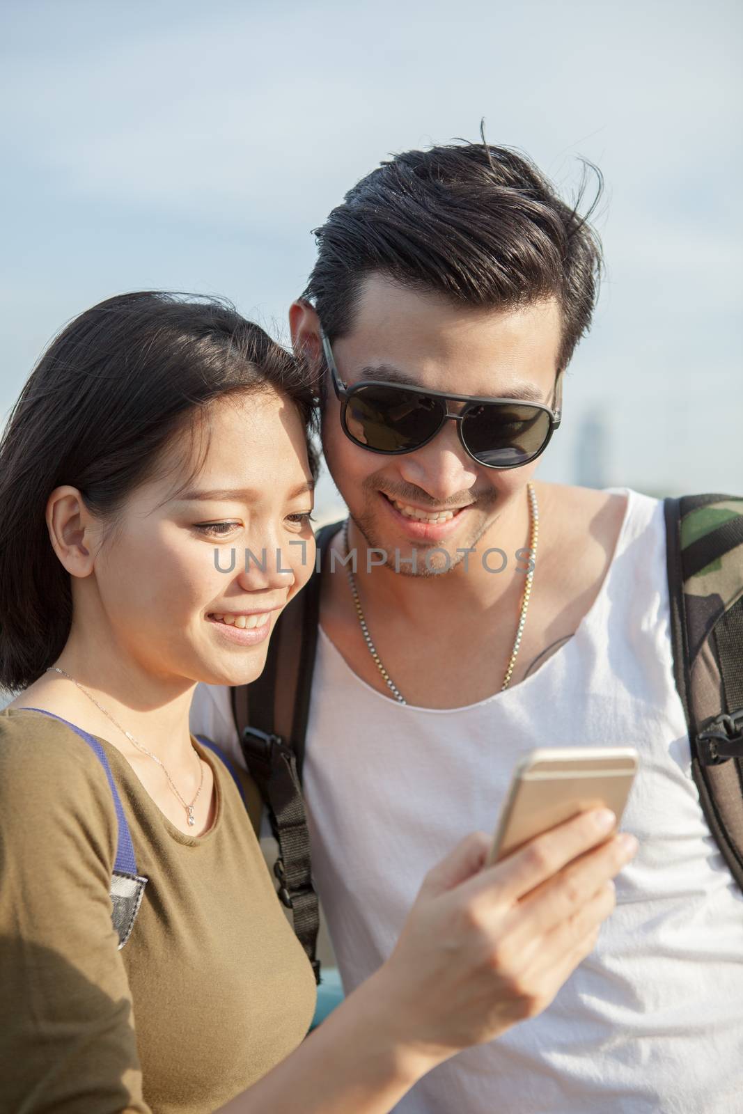 close up face of younger asian man and woman looking to smart ph by khunaspix