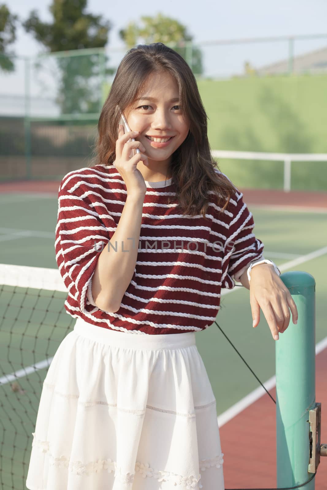 portrait of young beautiful asian woman talking smartphone in tennis course sport field use for modern life and digital telecommunication technology