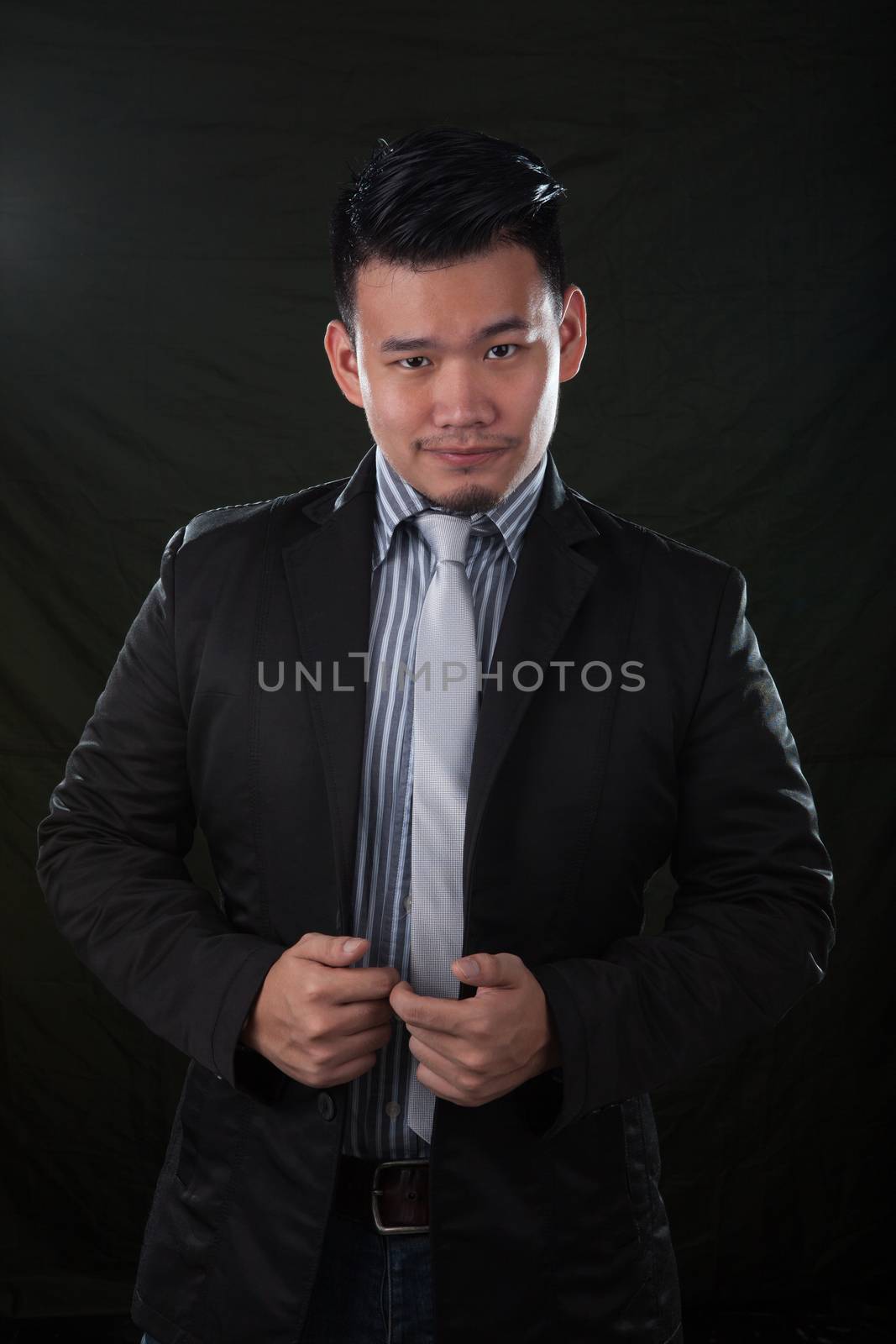 portrait smiling face with successful happiness emotion young asian man wearing western suit against black background with studio lighting 