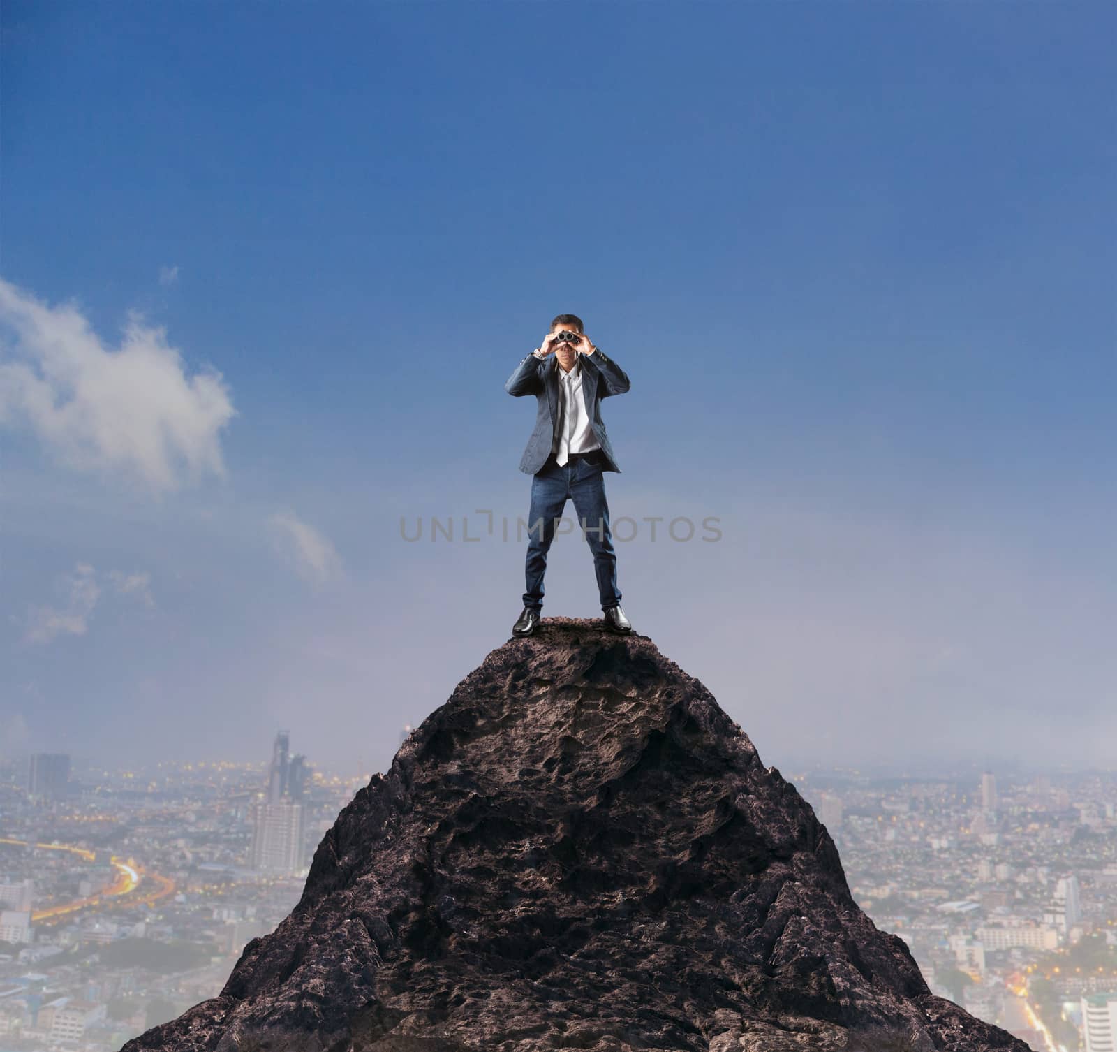 young business man standing on top of mountain and spying by binocular looking for something