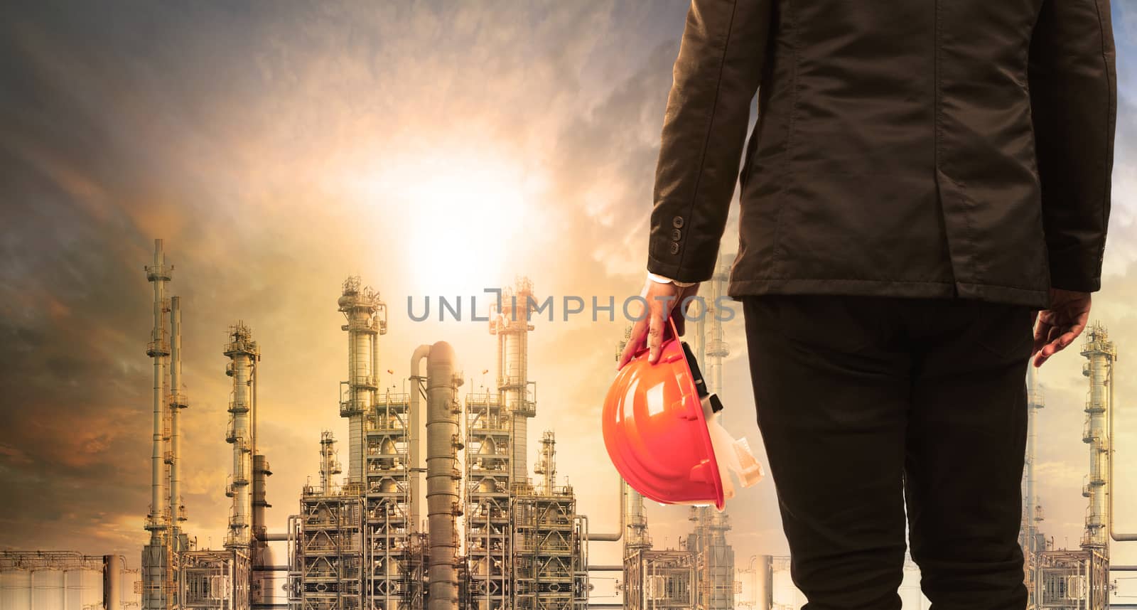 engineering man with safety helmet standing in industry estate against sun rising above oil refinery plant 