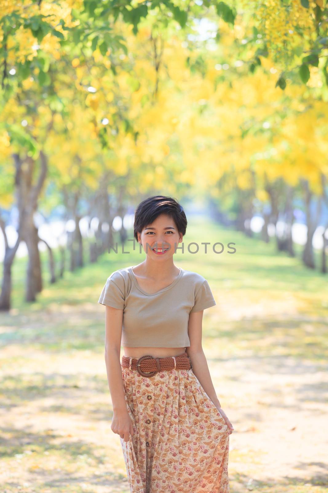 portrait of young and beautiful asian woman standing in park with  yellow blooming flowers plant and  happiness emotion