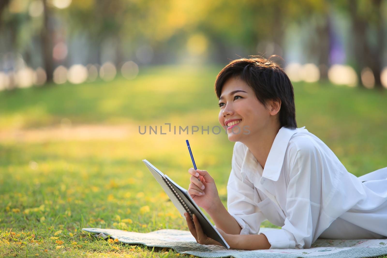 young woman lying on green grass park with pencil and note book in hand thinking something ,project,dream,hope,solution in future