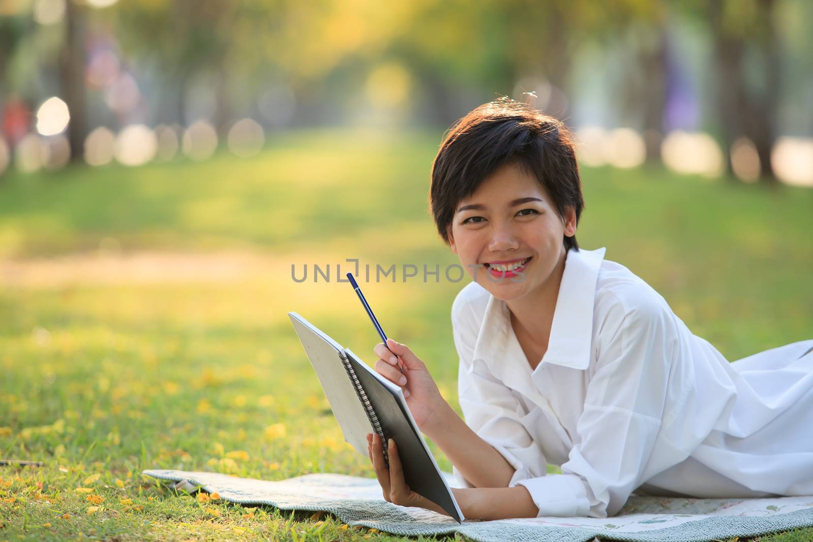 young woman lying on green grass park with pencil and note book in hand thinking something ,project,dream,hope,solution in future