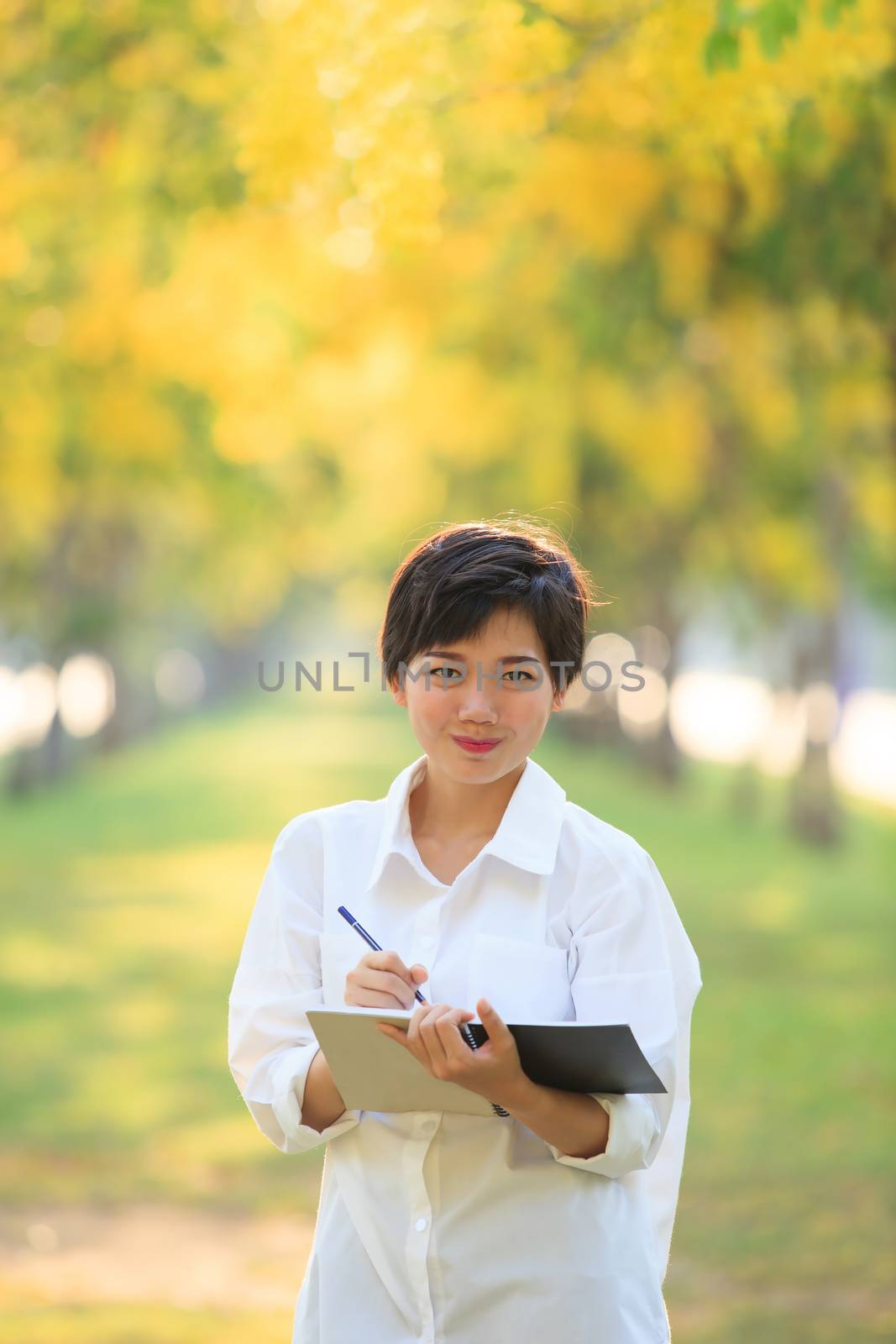 portrait of beautiful asian young woman staning in yellow flowers blooming park with writing tool for note some project ,check list something to do 
