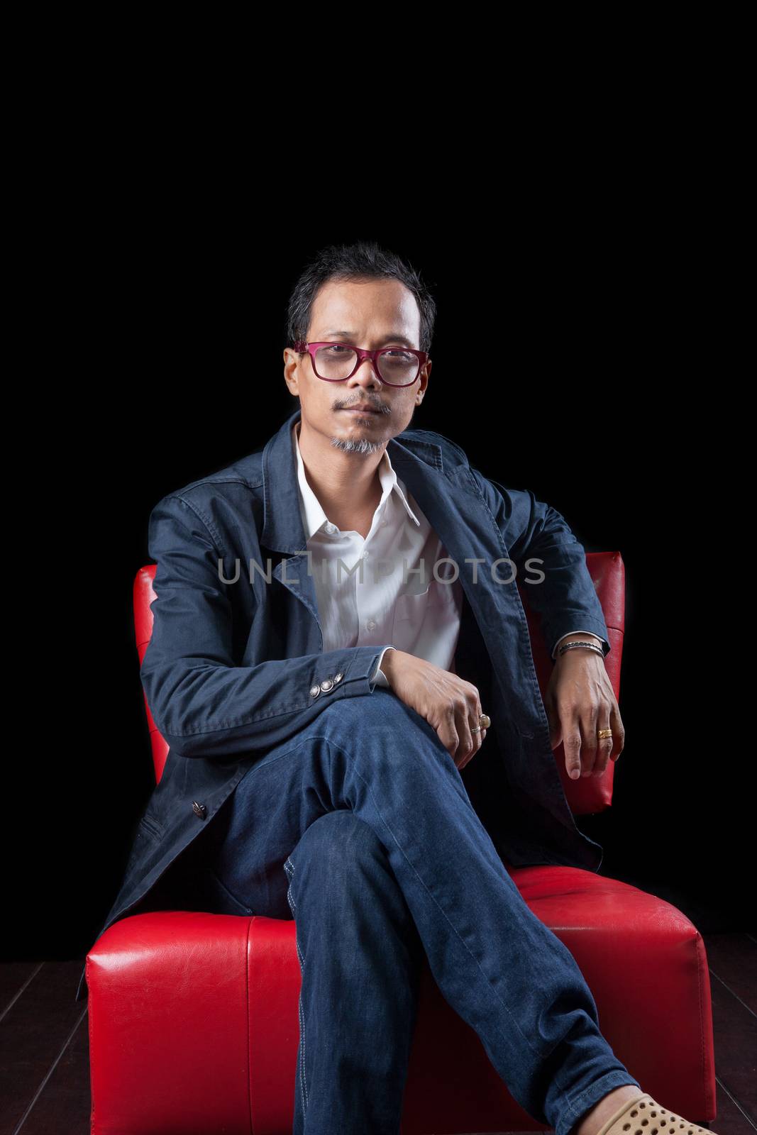 portrait face of 45s years old asian man sitting on red sofa in dark room with studio lighting photography
