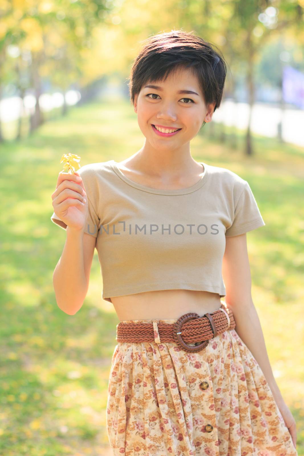 portrait of young and beautiful asian woman standing in park with little flowers in hand smiling to camera happiness emotion