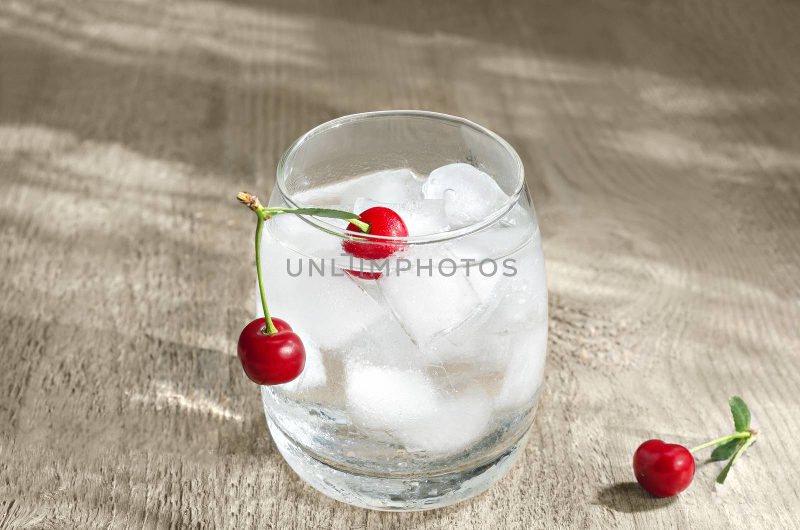 Cold water with ice and a cherry, is in the glass on wooden rough surfaces. Selective focus.