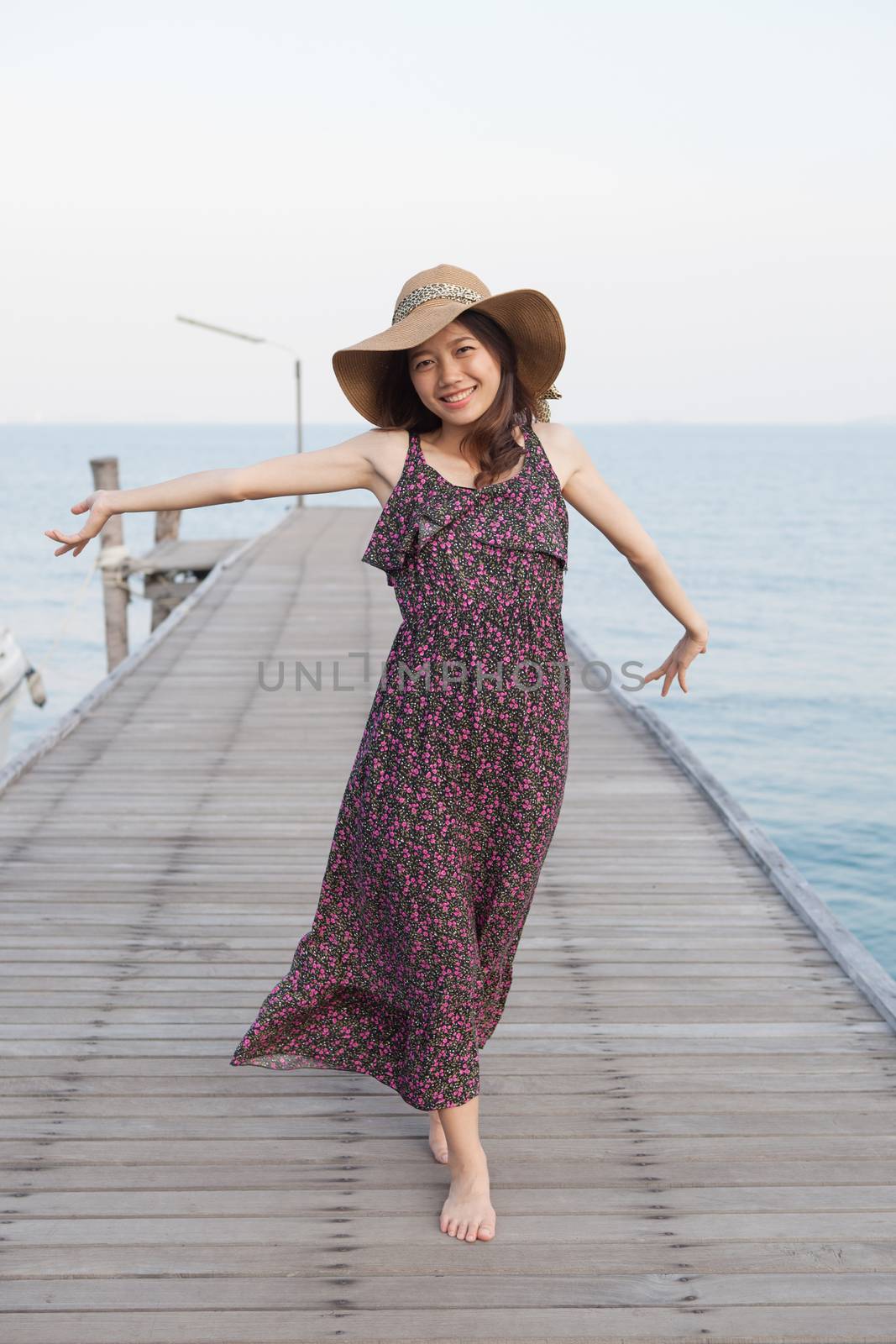 portrait of beautiful young woman wearing wide straw hat and long dress standing with happiness emotion on piers at sea beach 