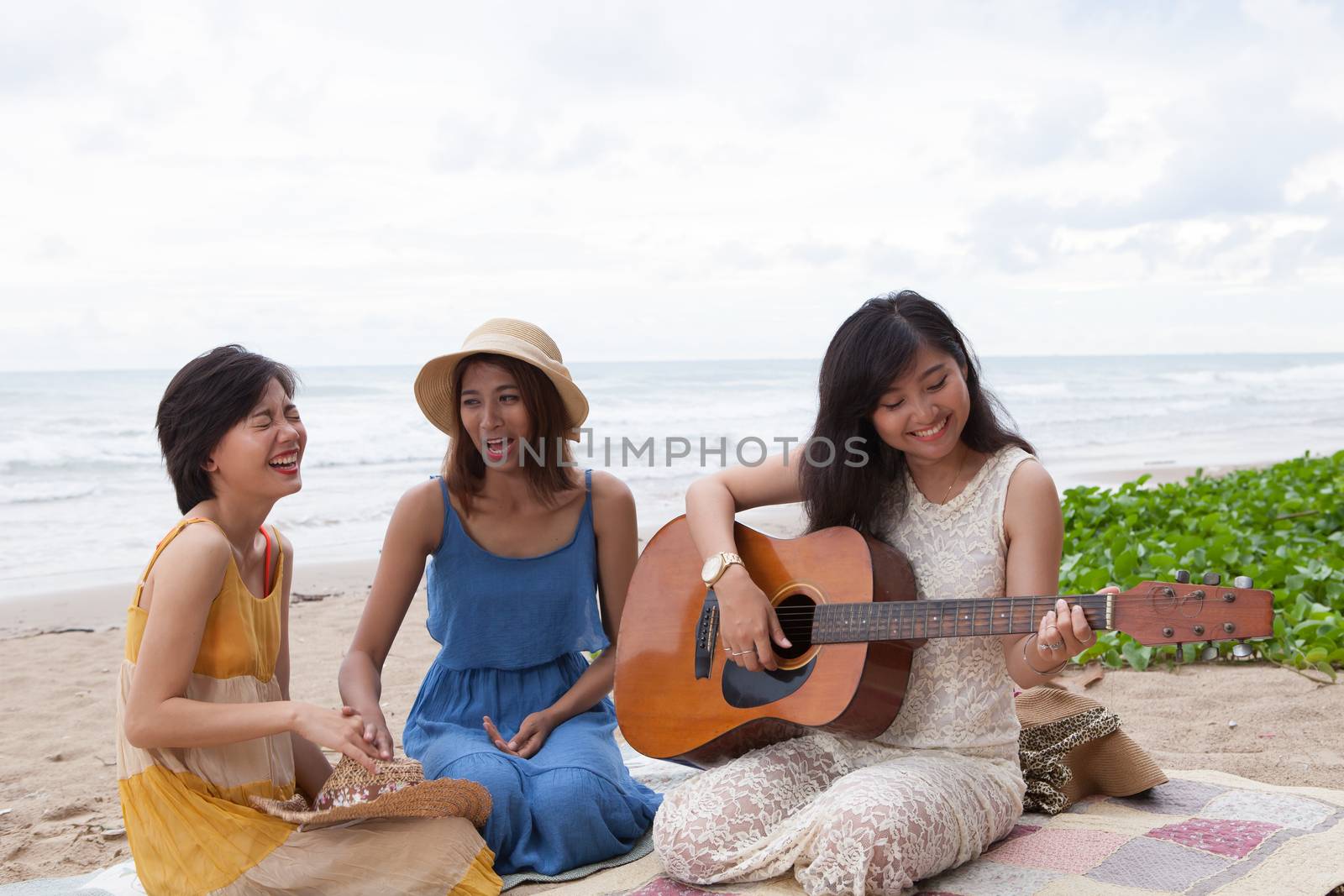 portrait group of young asian woman playing guitar in sea beach picnic party at sea side with happiness face emotion 