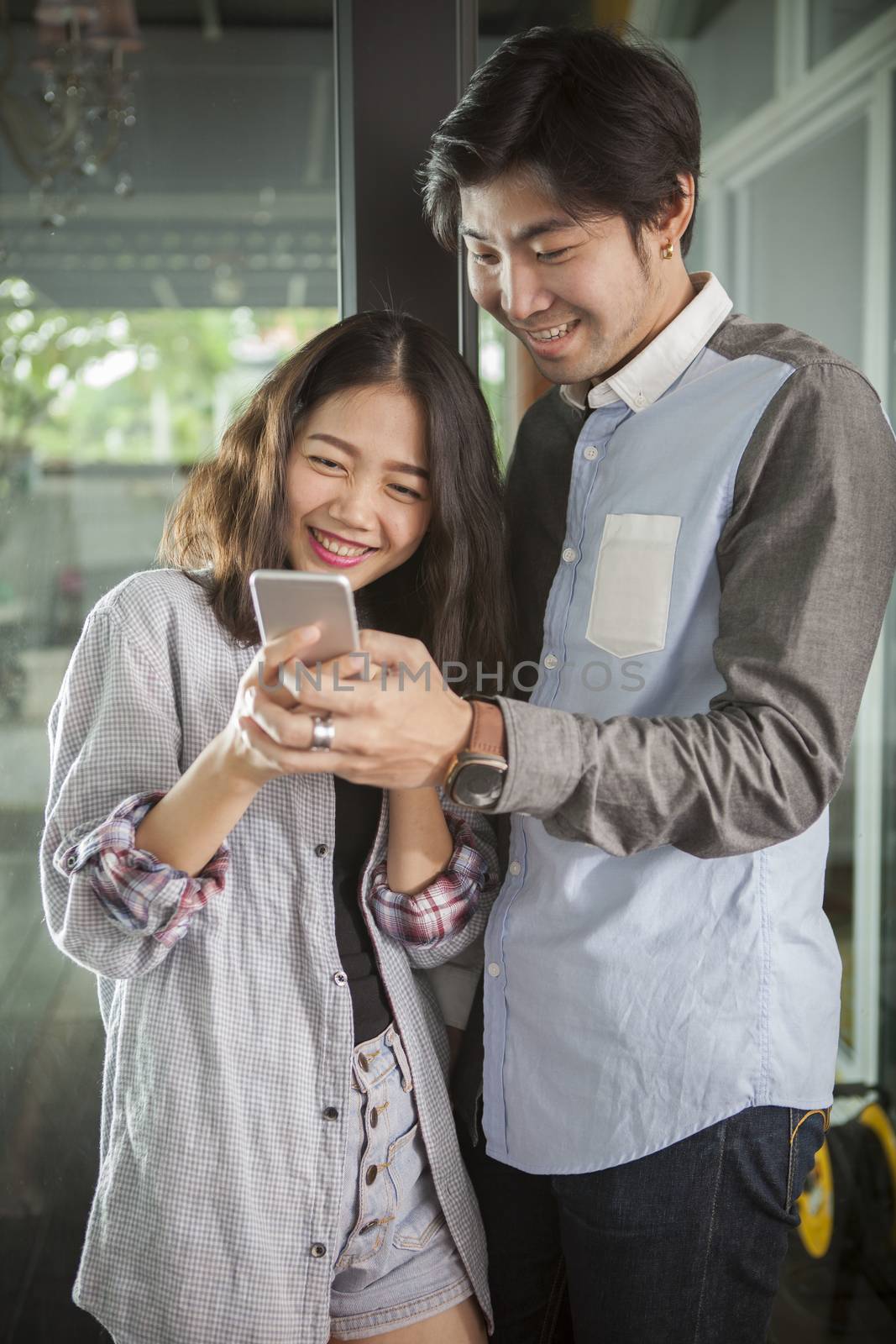 asian younger man and woman watching on smart phone with happy f by khunaspix