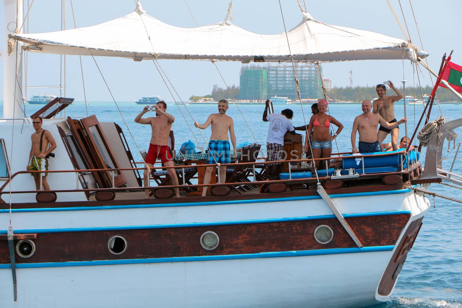MALE, MALDIVES- FEBRUARY 09, 2013: Old classic wooden boat without sails in open water. View on beautiful sailing ship with happy people it, from behind sailboat going . by evolutionnow