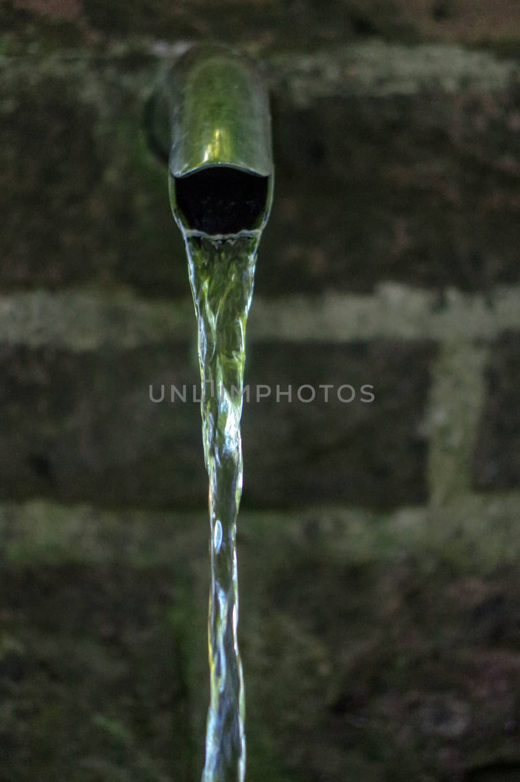 Close up of running water from a tap with brick wall in background