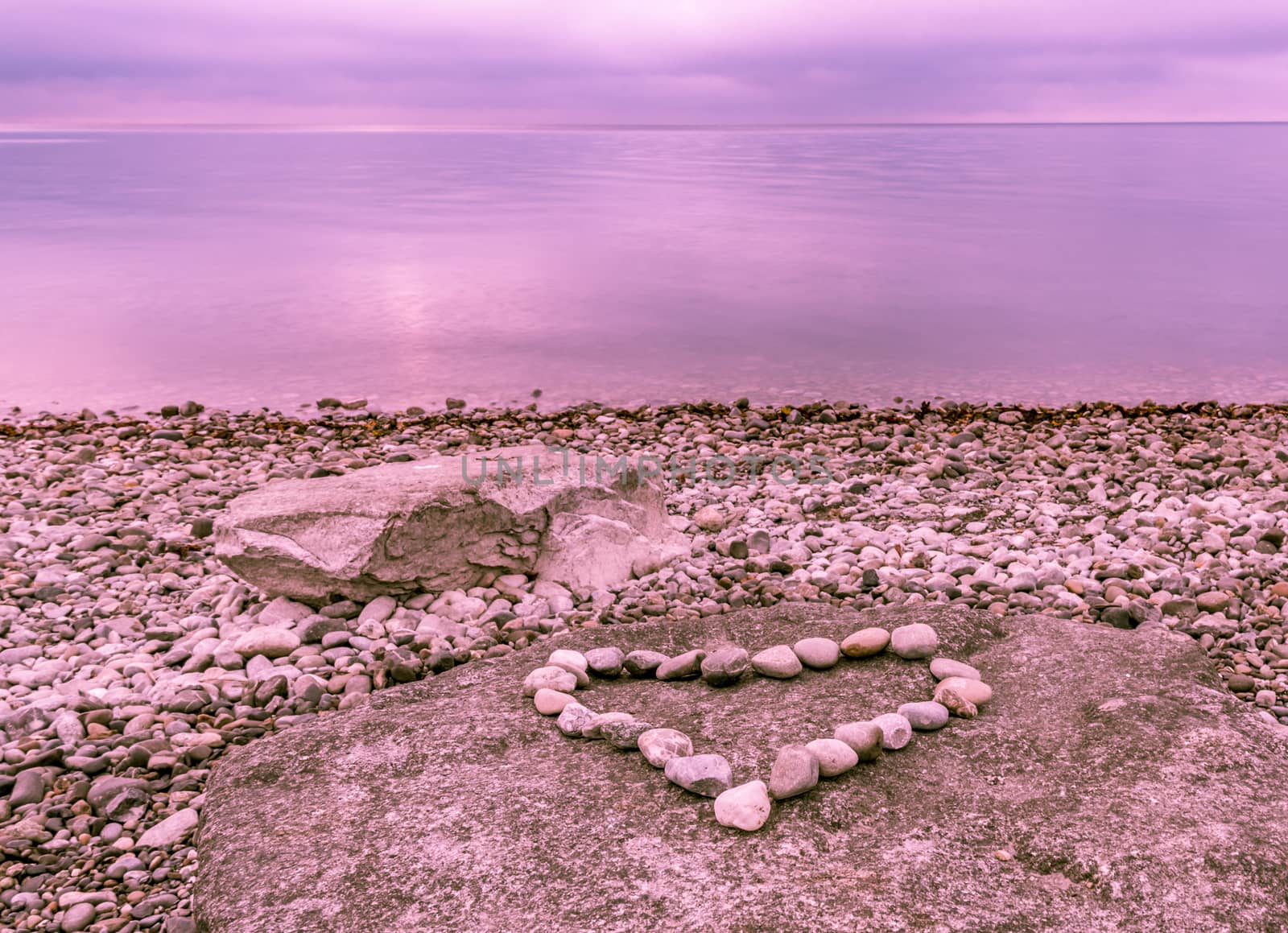 Heart shape made from stones placed on a big rock, near the lake Bodensee under a blue-purple sky, reflected in the water.