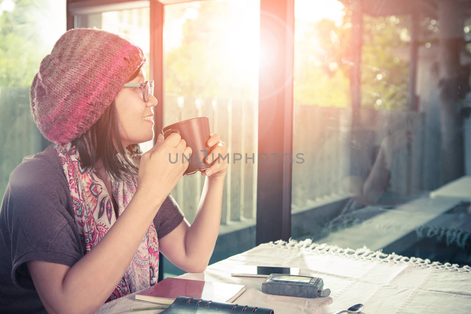 asian younger woman and hot coffee mug in hand smiling with happiness emotion sitting beside mirror window against beautiful sun light ,process warming color mood and tone