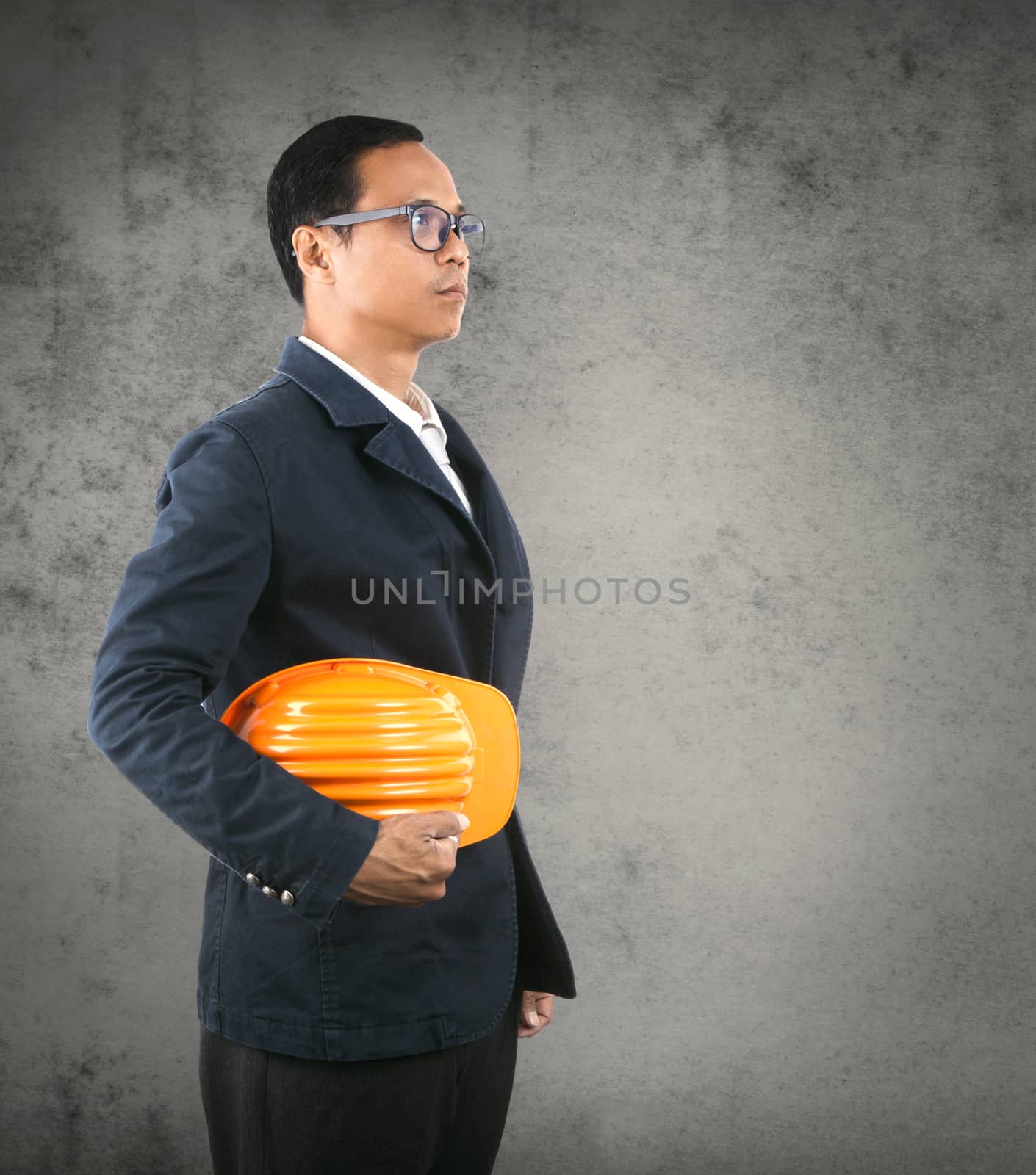 portrait of self conficence engineering man holding safety helmet against cement wall