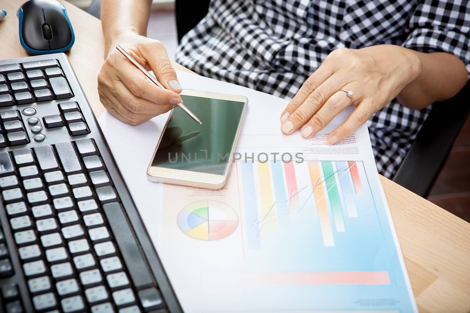 woman writing with smart phone pen on mobile phone screen with business graph report on table use as people working by internet technology