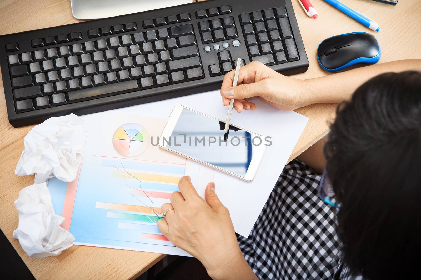woman watching to smart phone touching screen and writing with business report graph on working table and paper crumpled beside use for people business decision concept