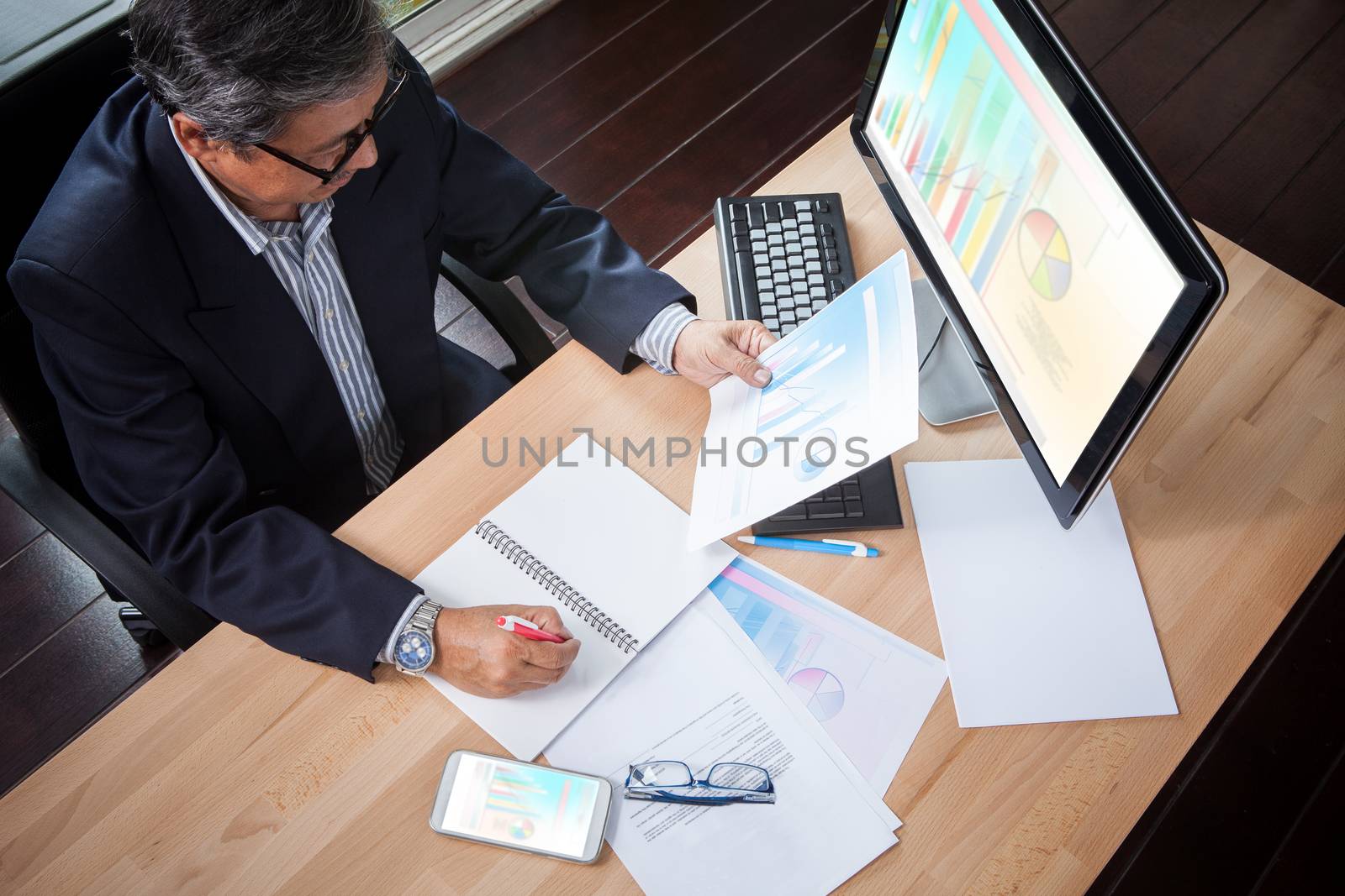 senior business man looking to business paper graph report in hand and writing strategy analysis plan on working table