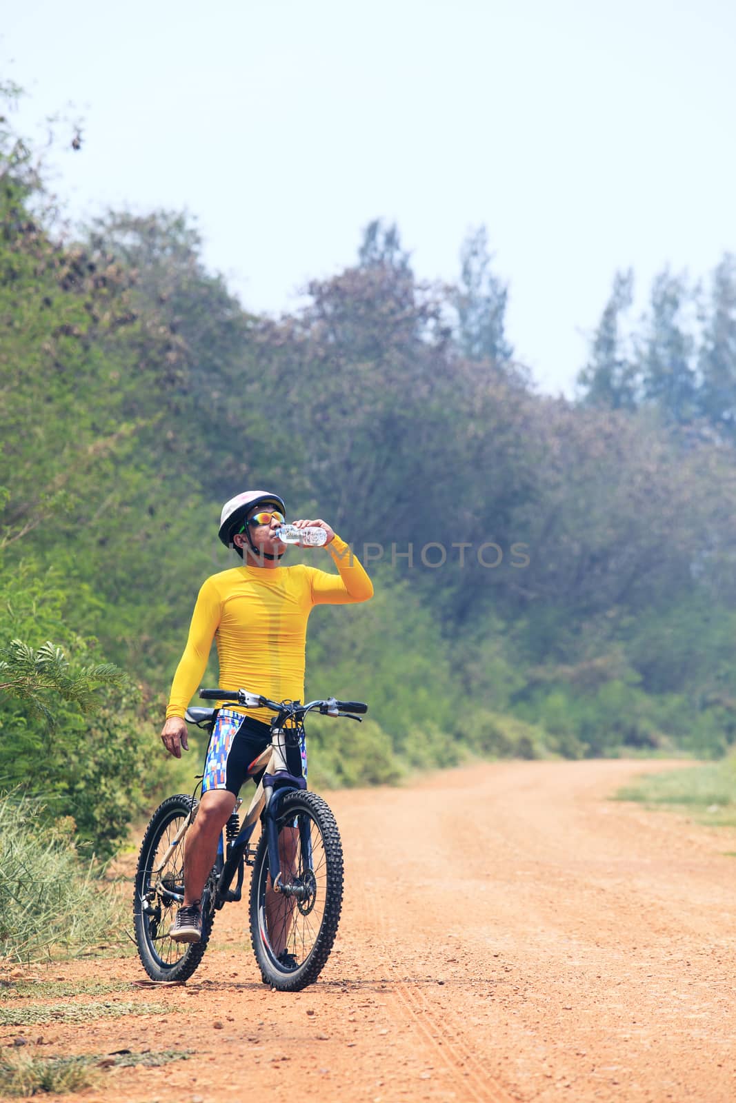 young bicycle (cyclist) man drinking fresh water from plastic bottle while biking mtb on dirty road  use for activities and sport hobby theme