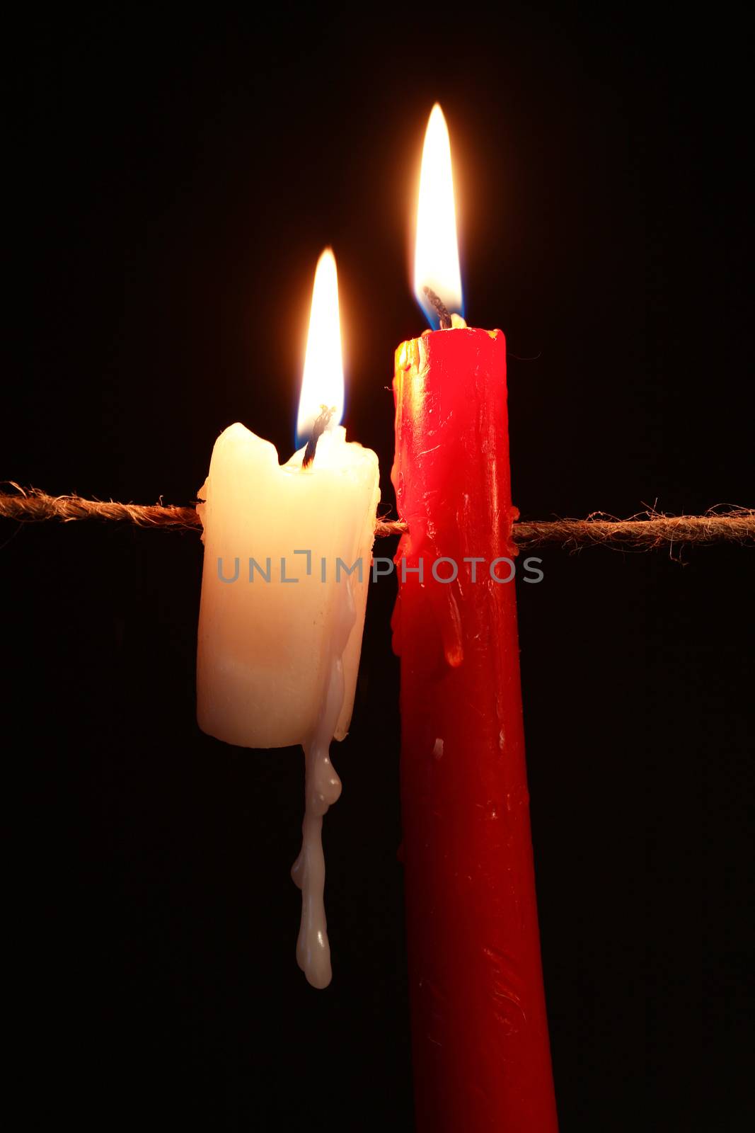 Pair of lighting candles hanging with rope against dark background