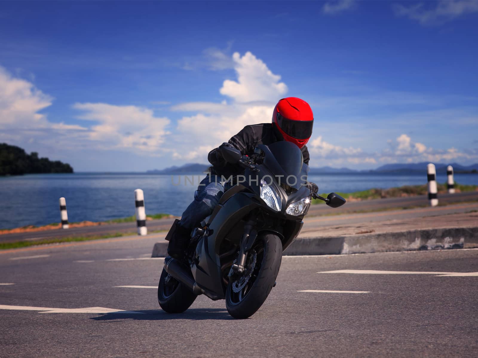 young biker man riding motorcycle on asphalt road against beautiful sea water background
