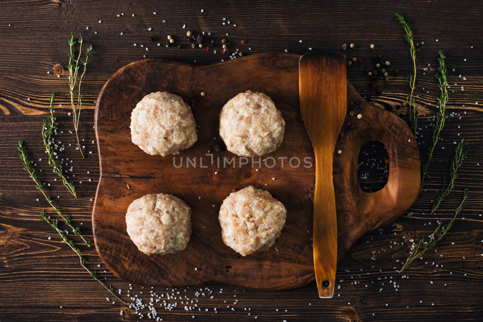 Uncooked meatballs on a dark wooden board by kzen