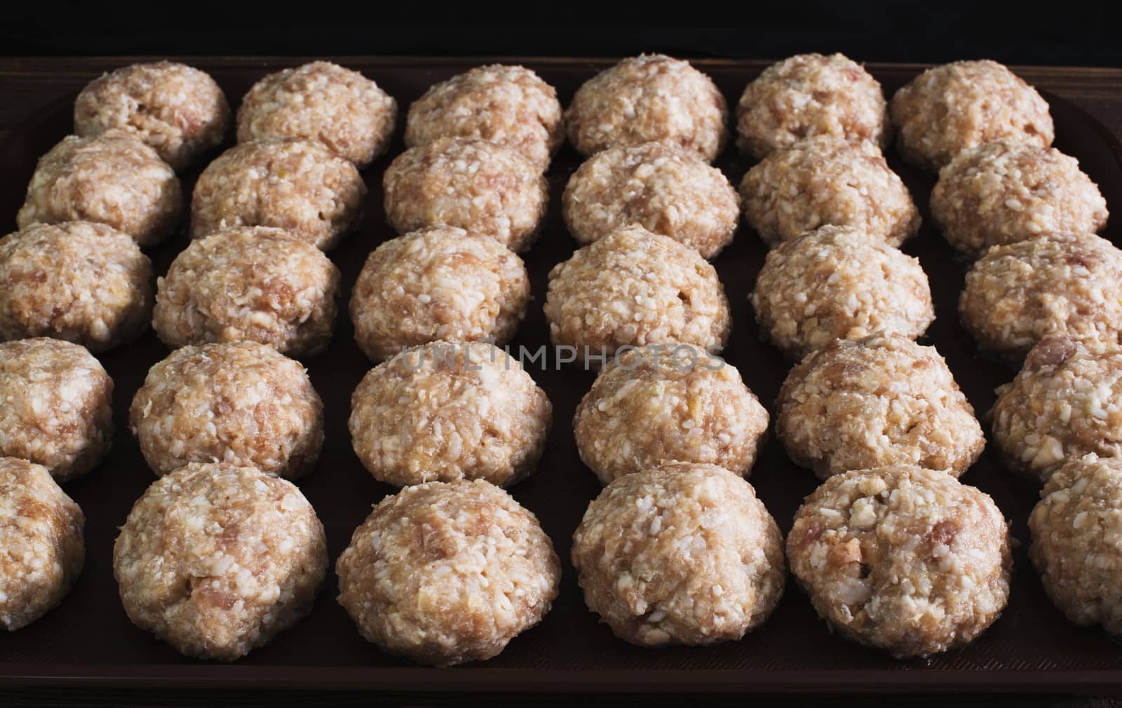 Lots uncooked meatballs on dark tray by kzen