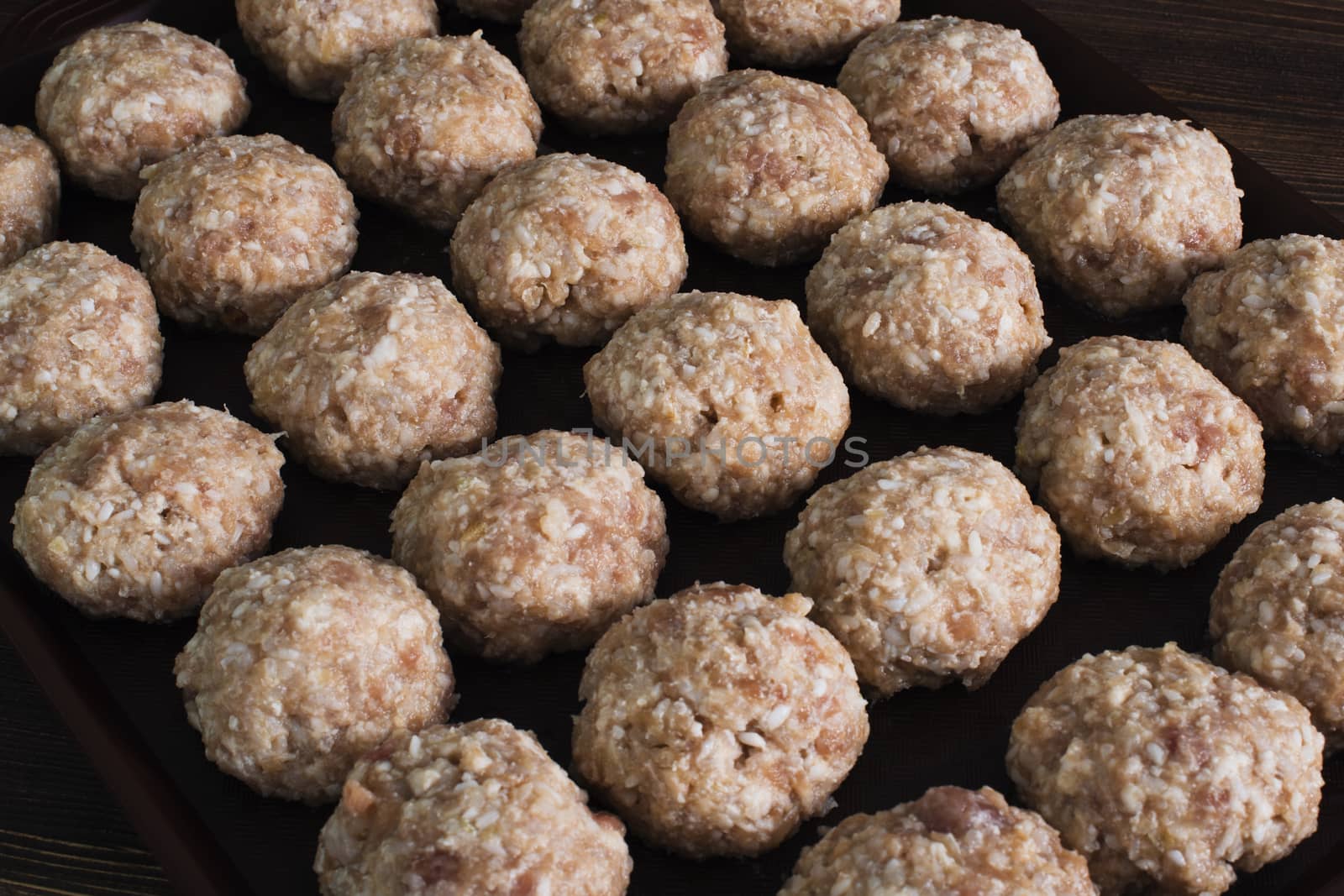Lots uncooked meatballs on dark tray by kzen