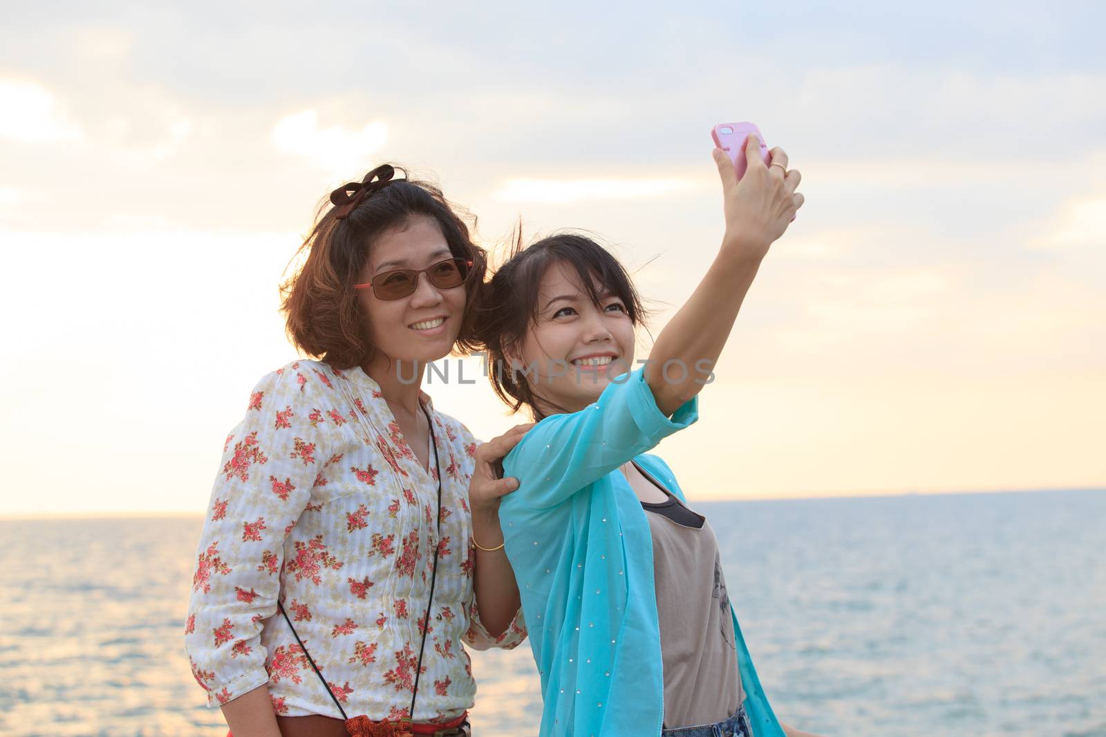 two sister take a photo,selfie by smart phone beside sea beach with happy emotion