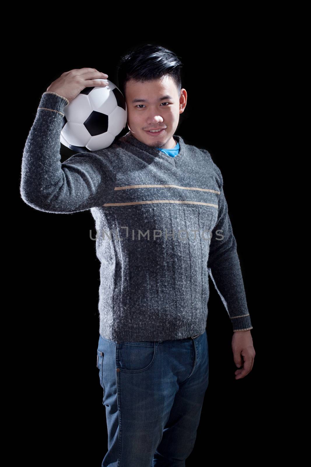 young man holding soccer football with smiling face standing aga by khunaspix
