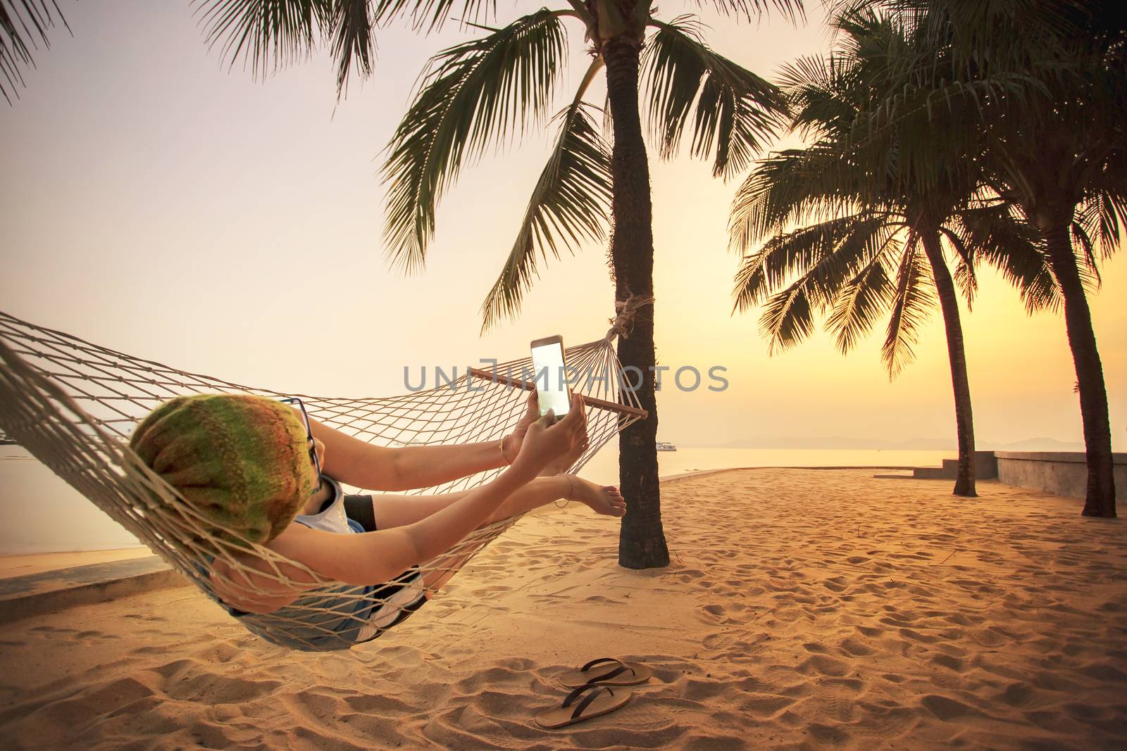 woman lying in beach cradle and taking a photograph by smart pho by khunaspix