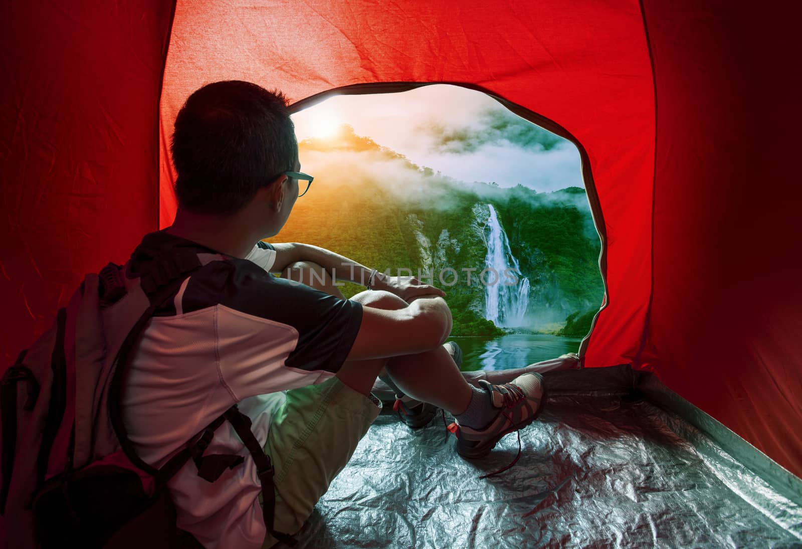 camping man in camper tent looking to beautiful natural water fa by khunaspix
