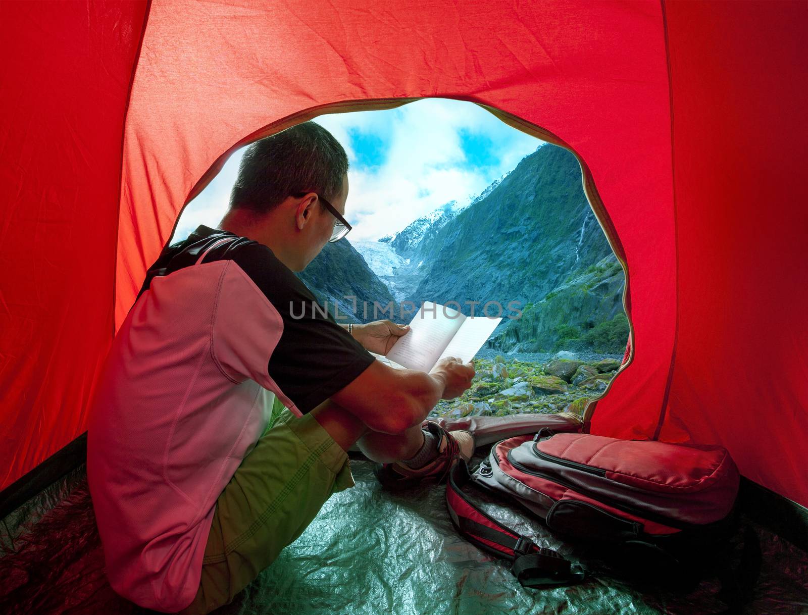 camping man reading traveling guide book in camp tent against be by khunaspix